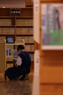 A person crouches down to look at books in a library.