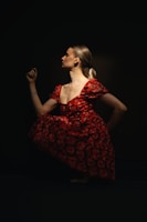 Woman poses in a red dress against a dark background.