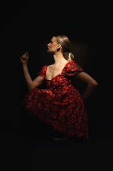 Woman poses in a red dress against a dark background.