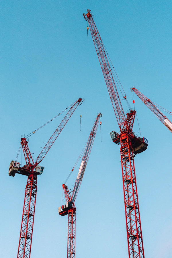 Construction cranes rising against a clear blue sky at an infrastructure build site