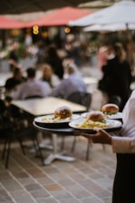 A waiter carries plates of burgers outside.