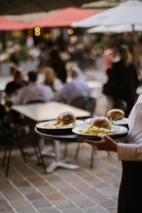 A waiter carries plates of burgers outside.