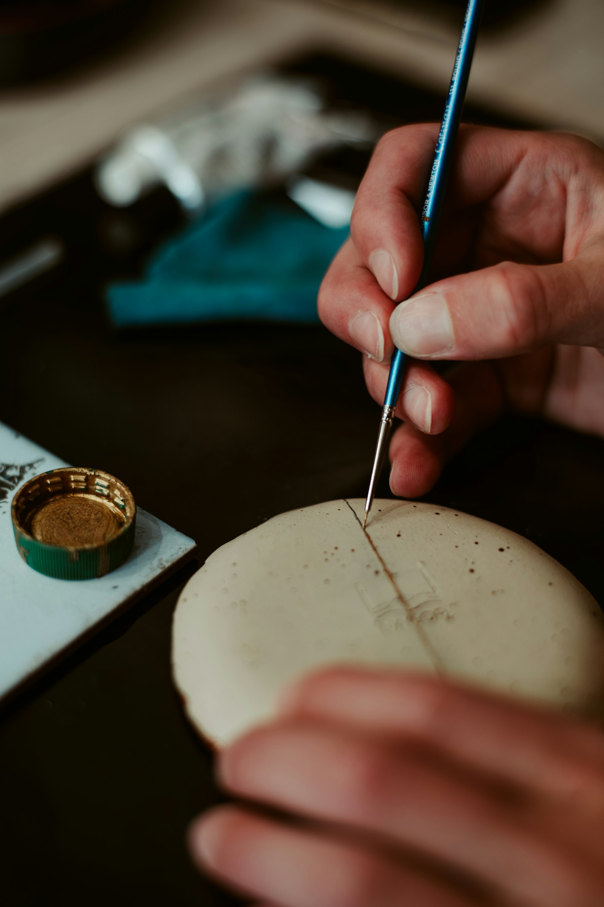 A hand paints a detail on a ceramic piece.