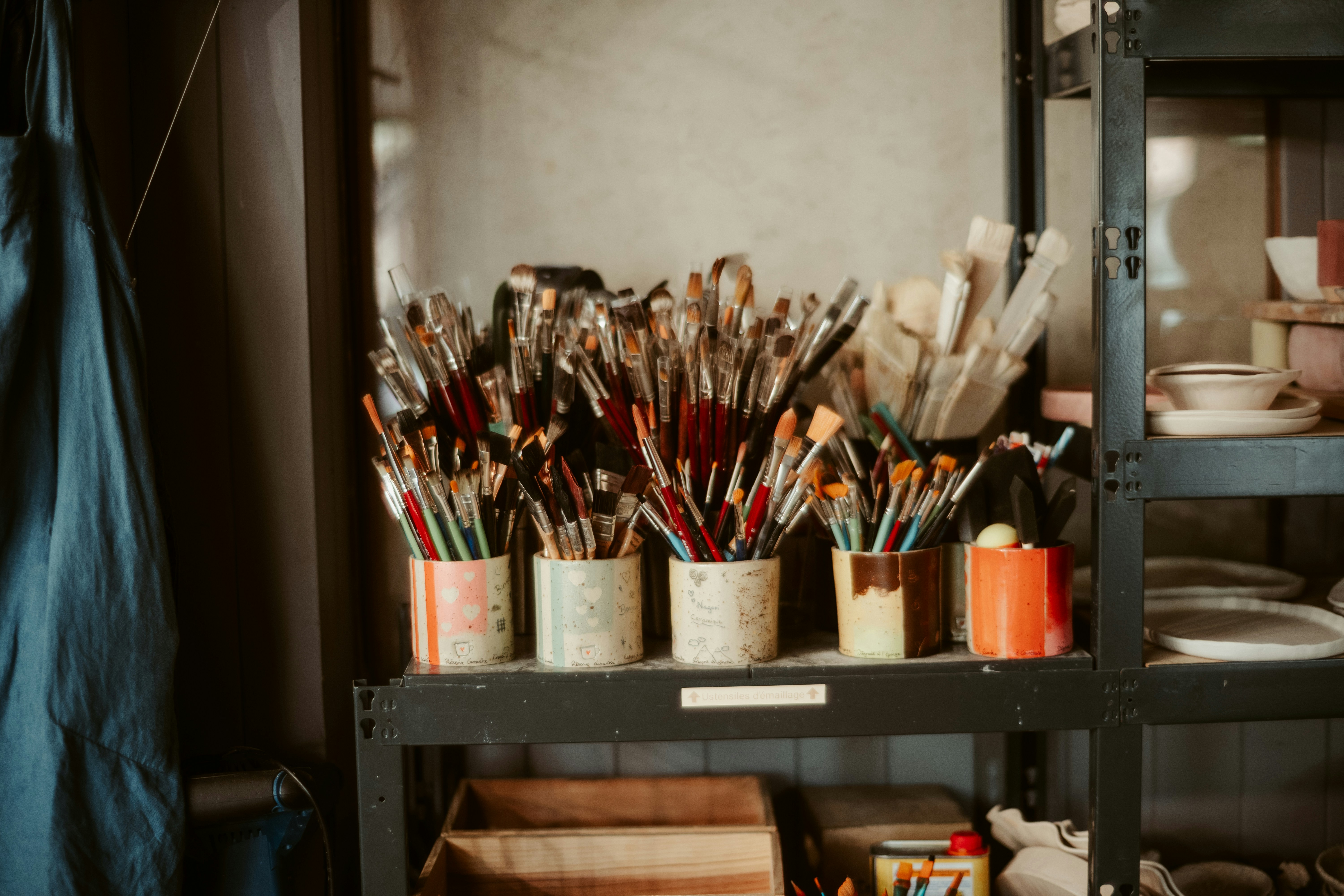 Paintbrushes are stored in cans on a shelf.