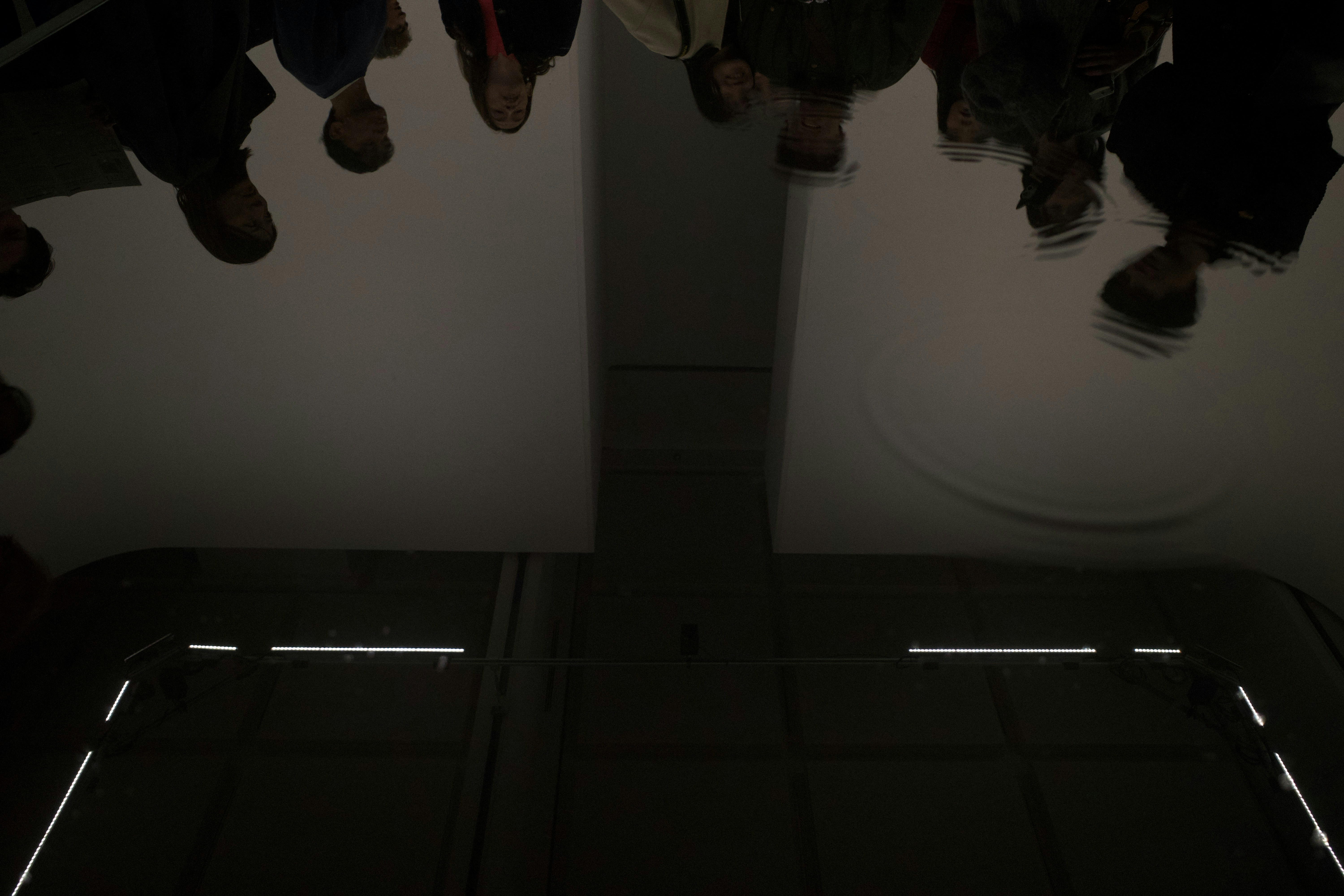 People are reflected on a dark, shiny surface.