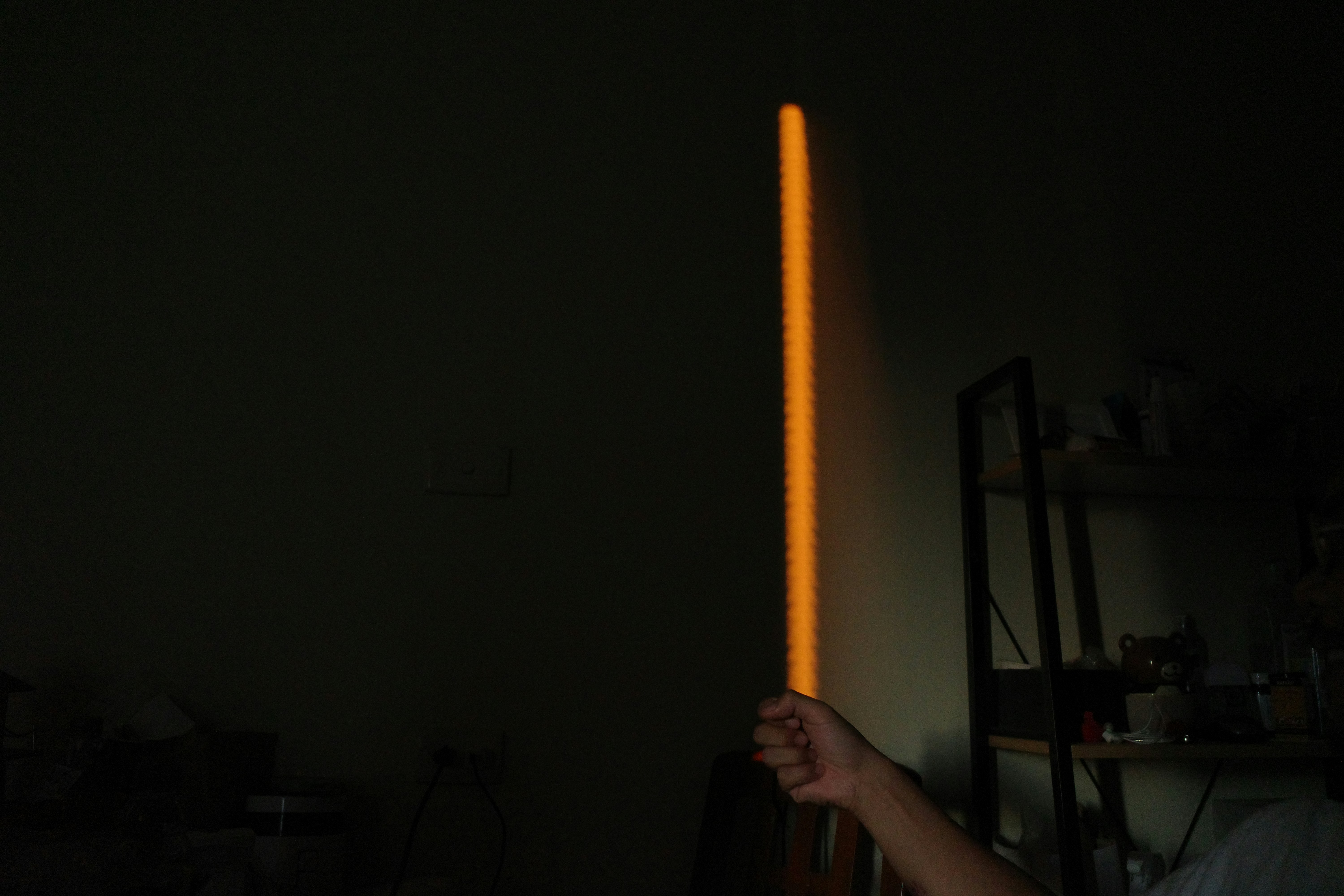 A hand holds a glowing orange lightsaber.