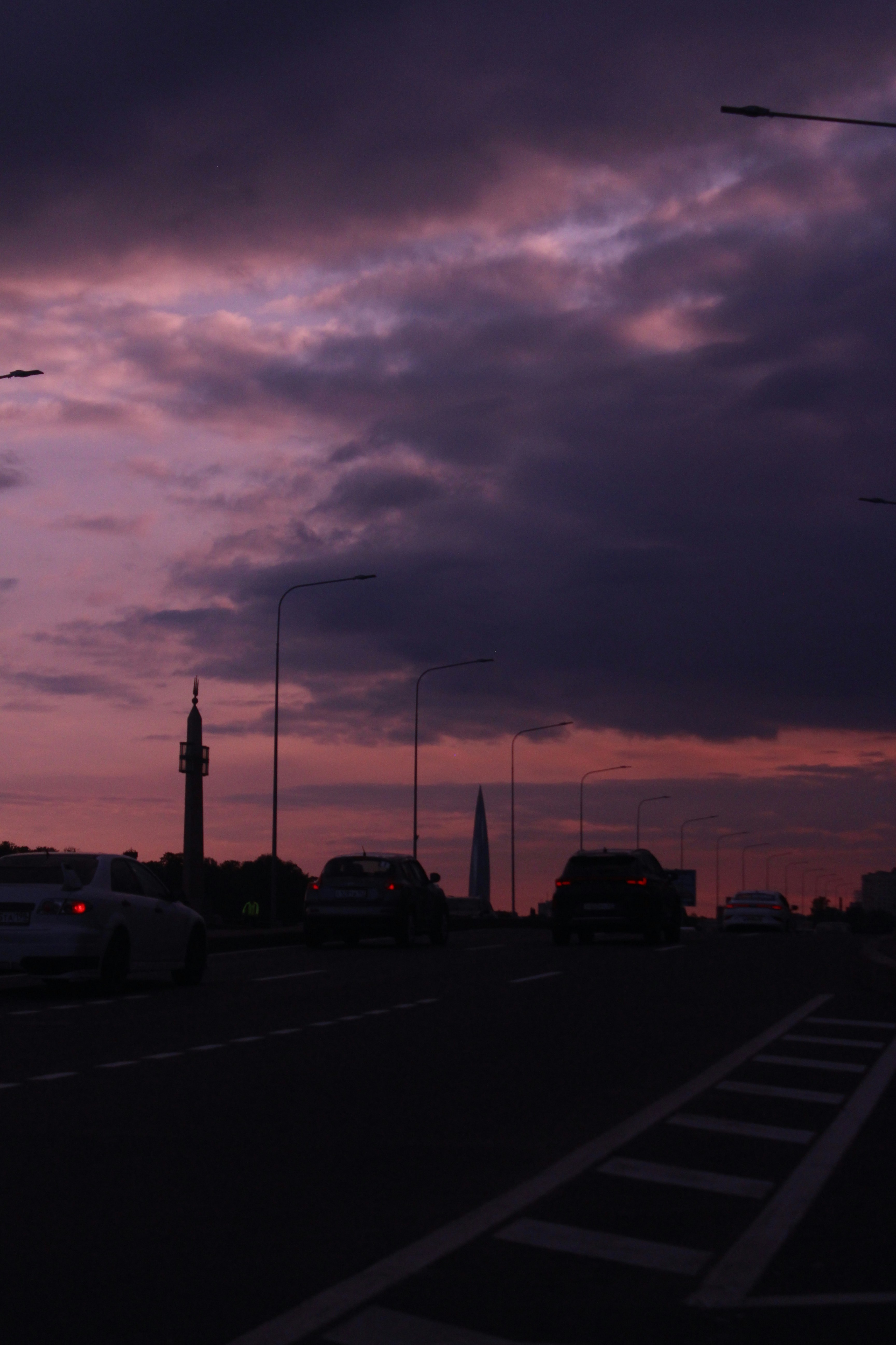 A purple sunset illuminates a city road.