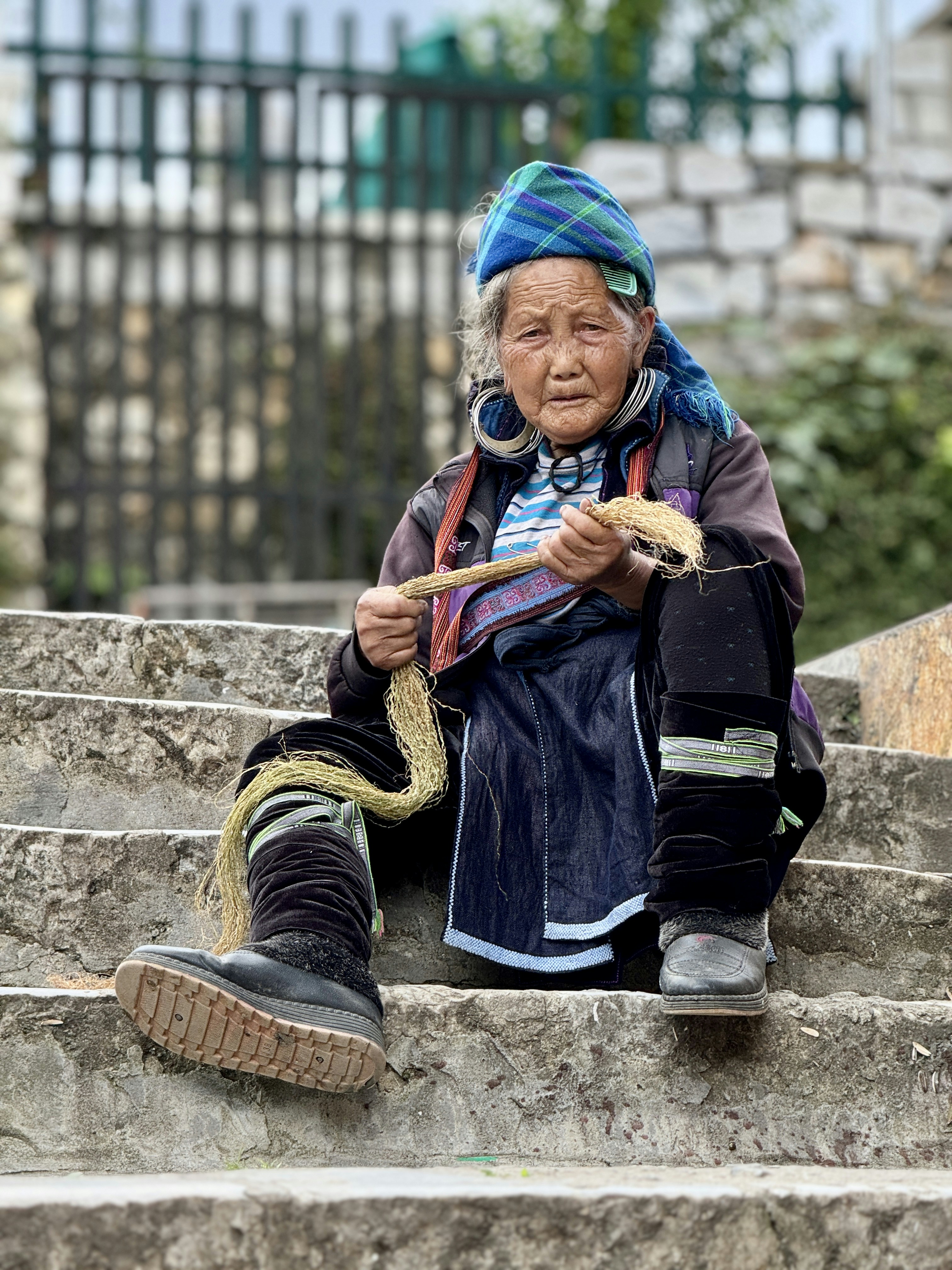 Uma mulher idosa senta-se em degraus, trabalhando com barbante.