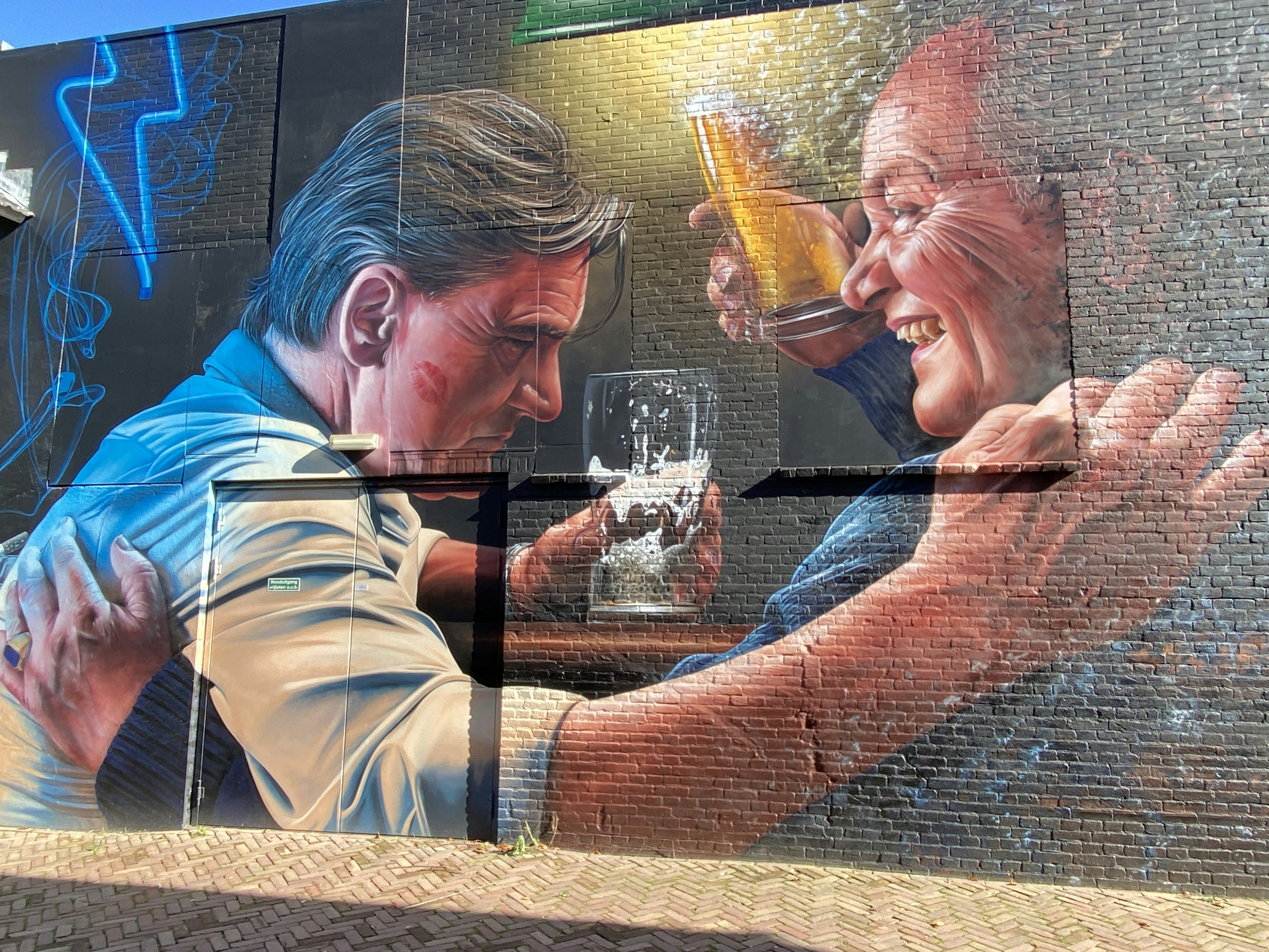 Duas pessoas tilintam copos em um mural comemorativo.