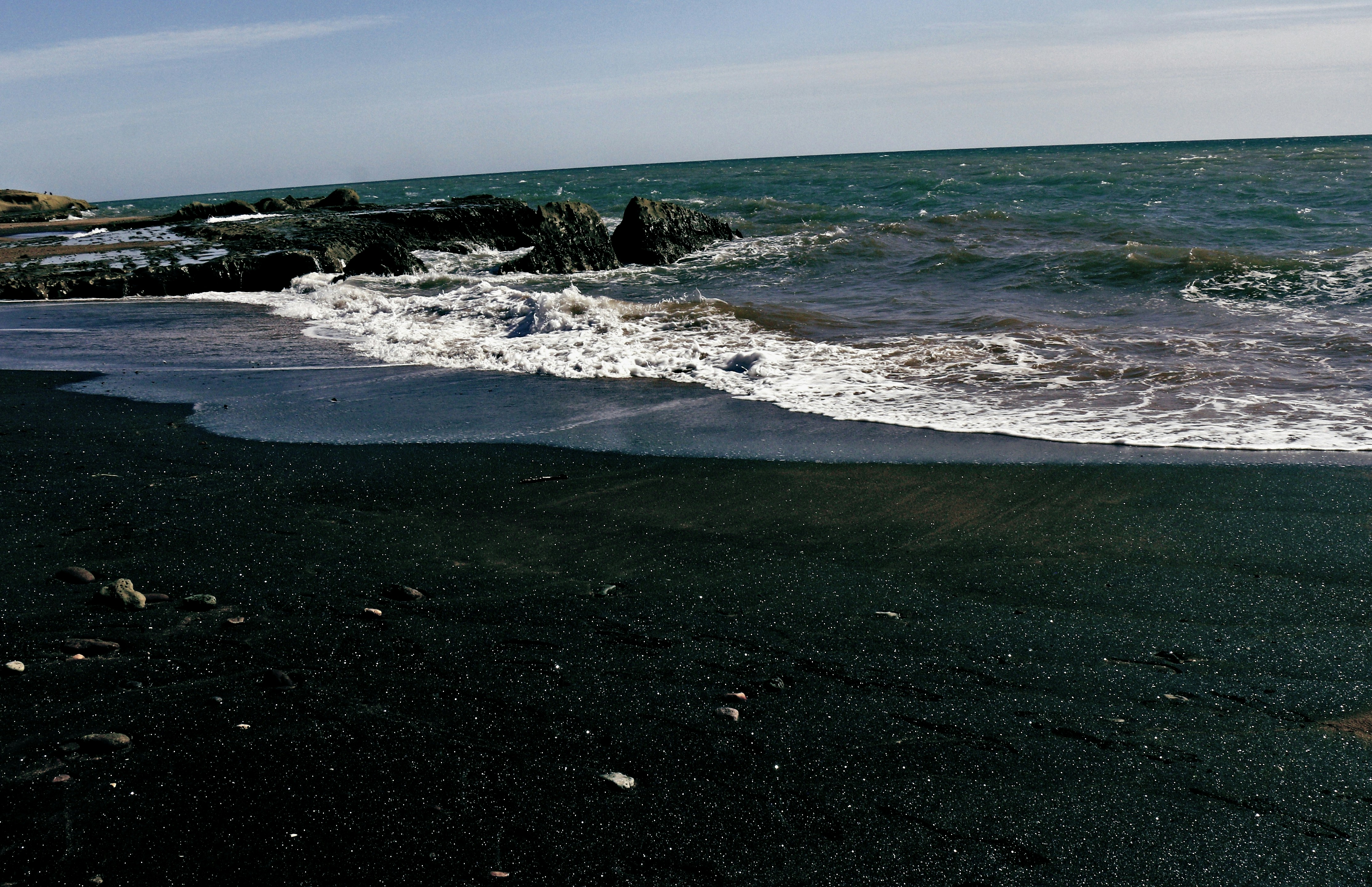 Waves crash on a dark, sandy beach.