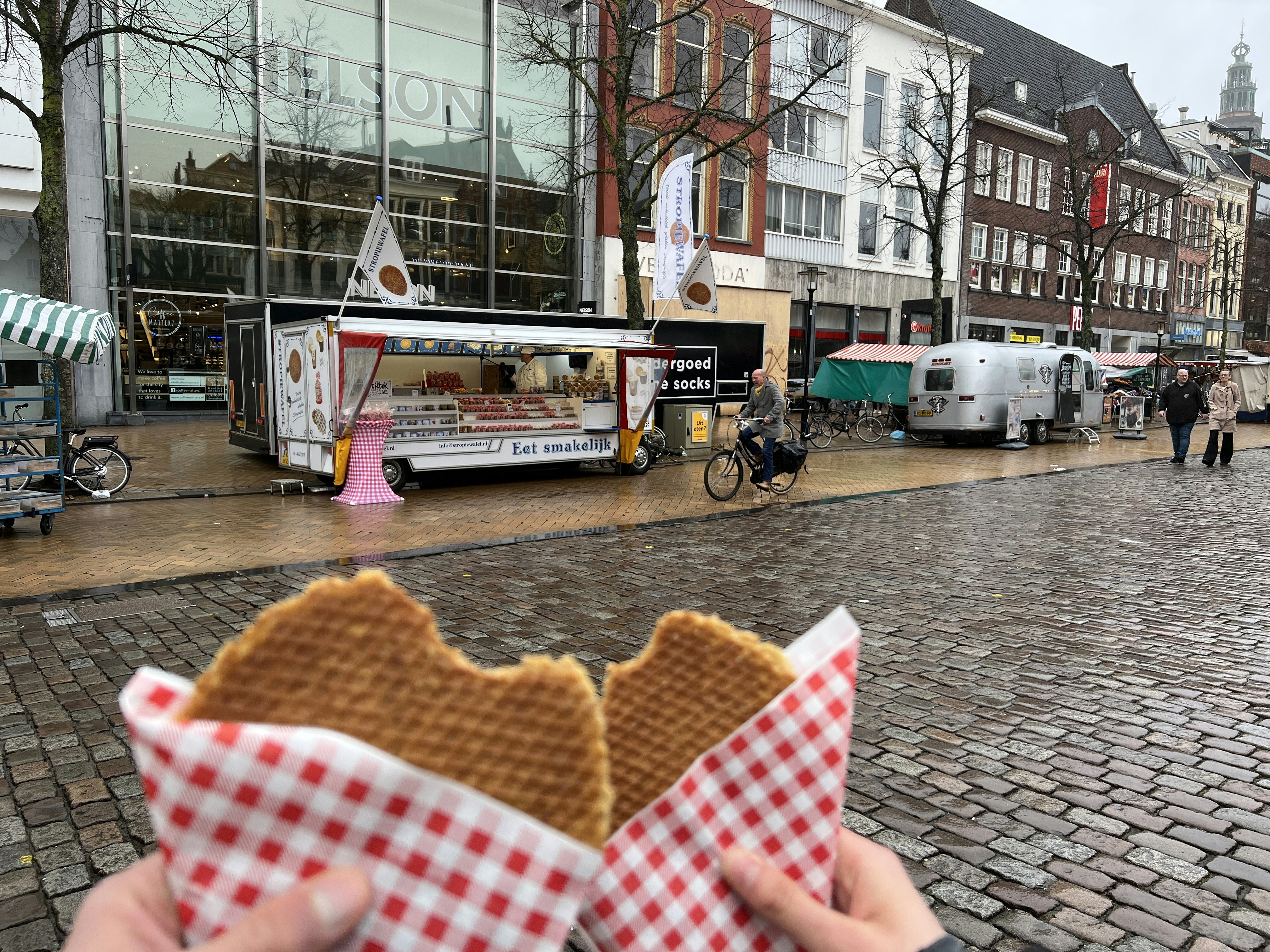 Hands hold waffles in front of a city food truck.