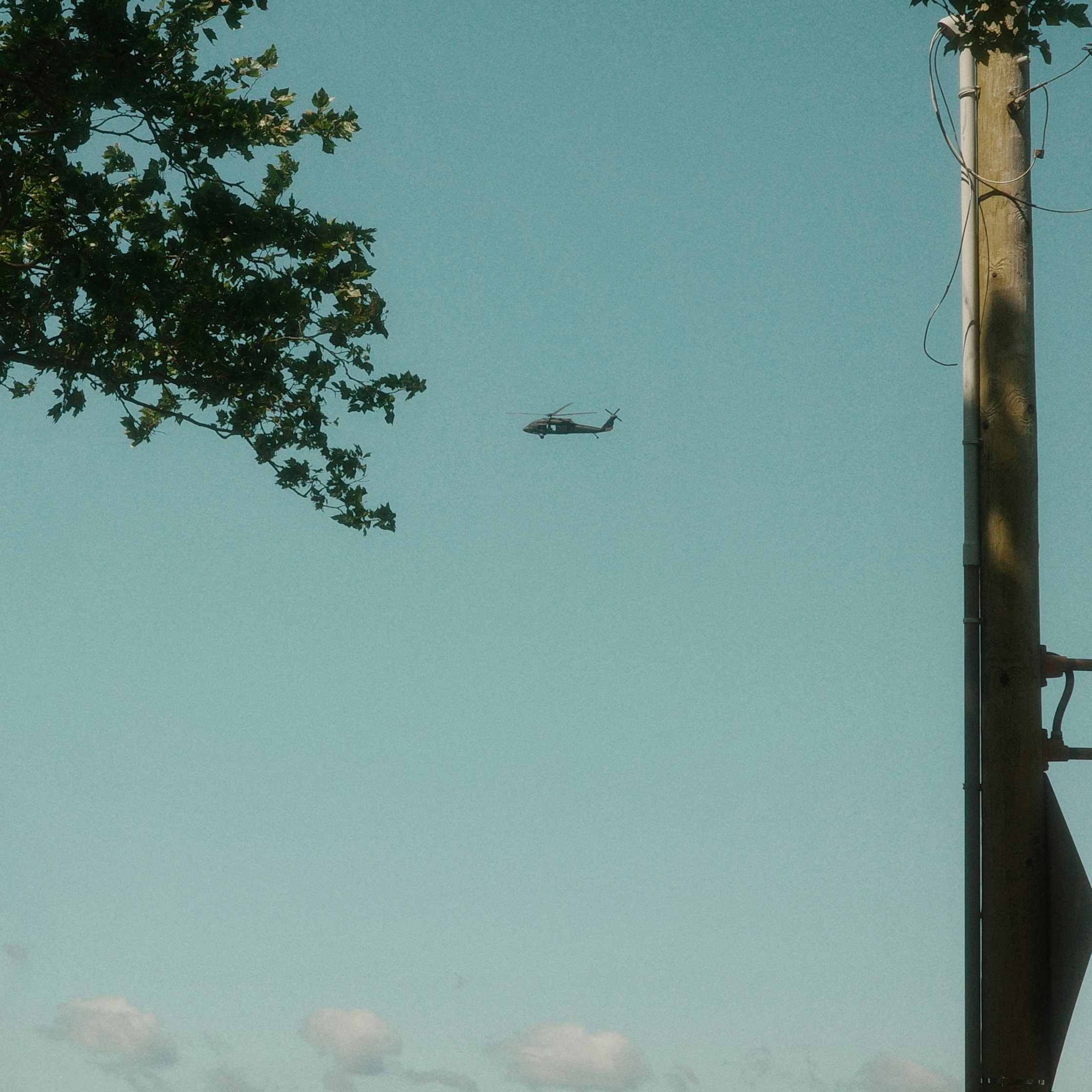 A helicopter flies high in a bright blue sky.