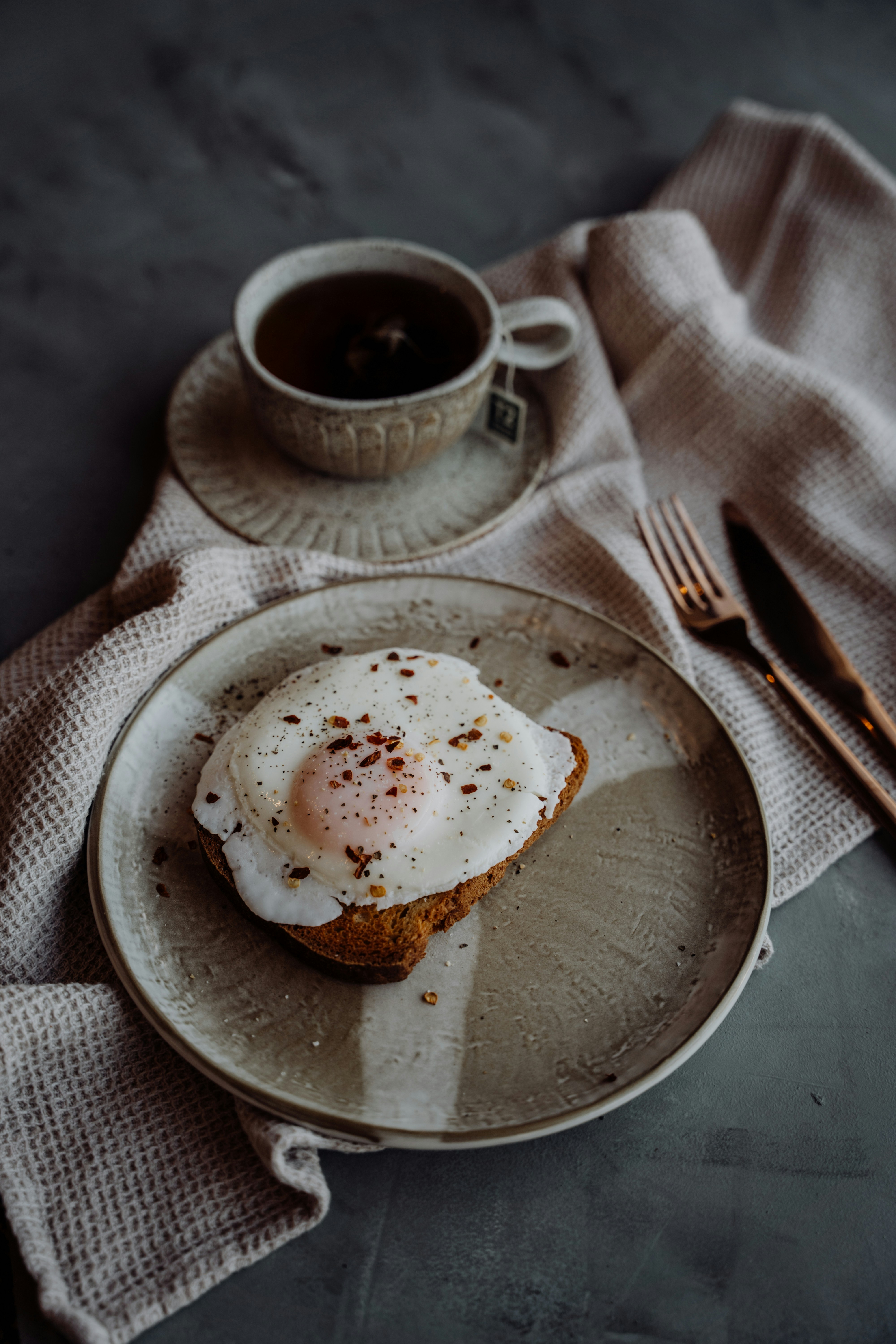 Fried egg on toast with tea and utensils.