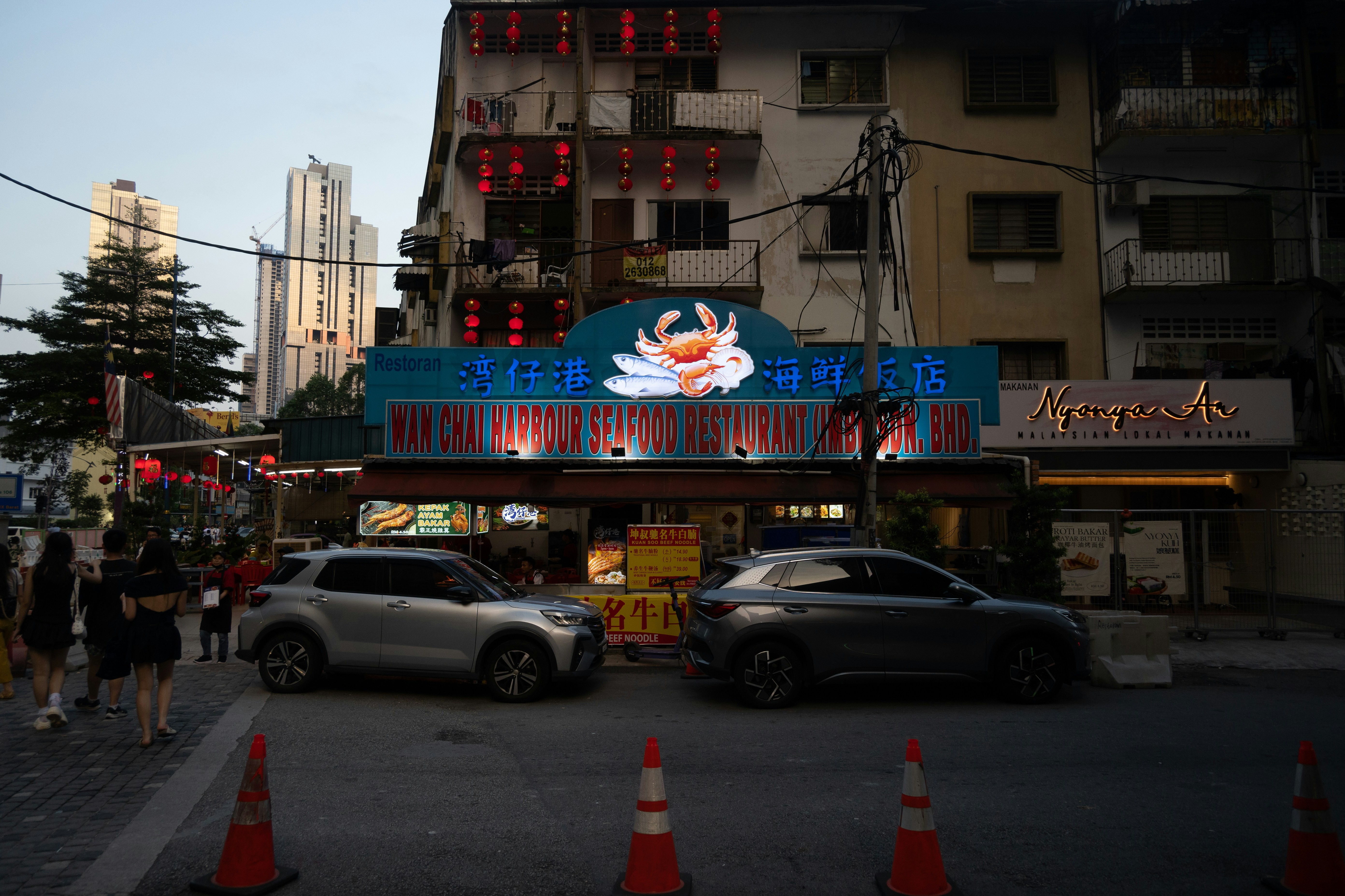 A restaurant with a lit sign and cars in front.