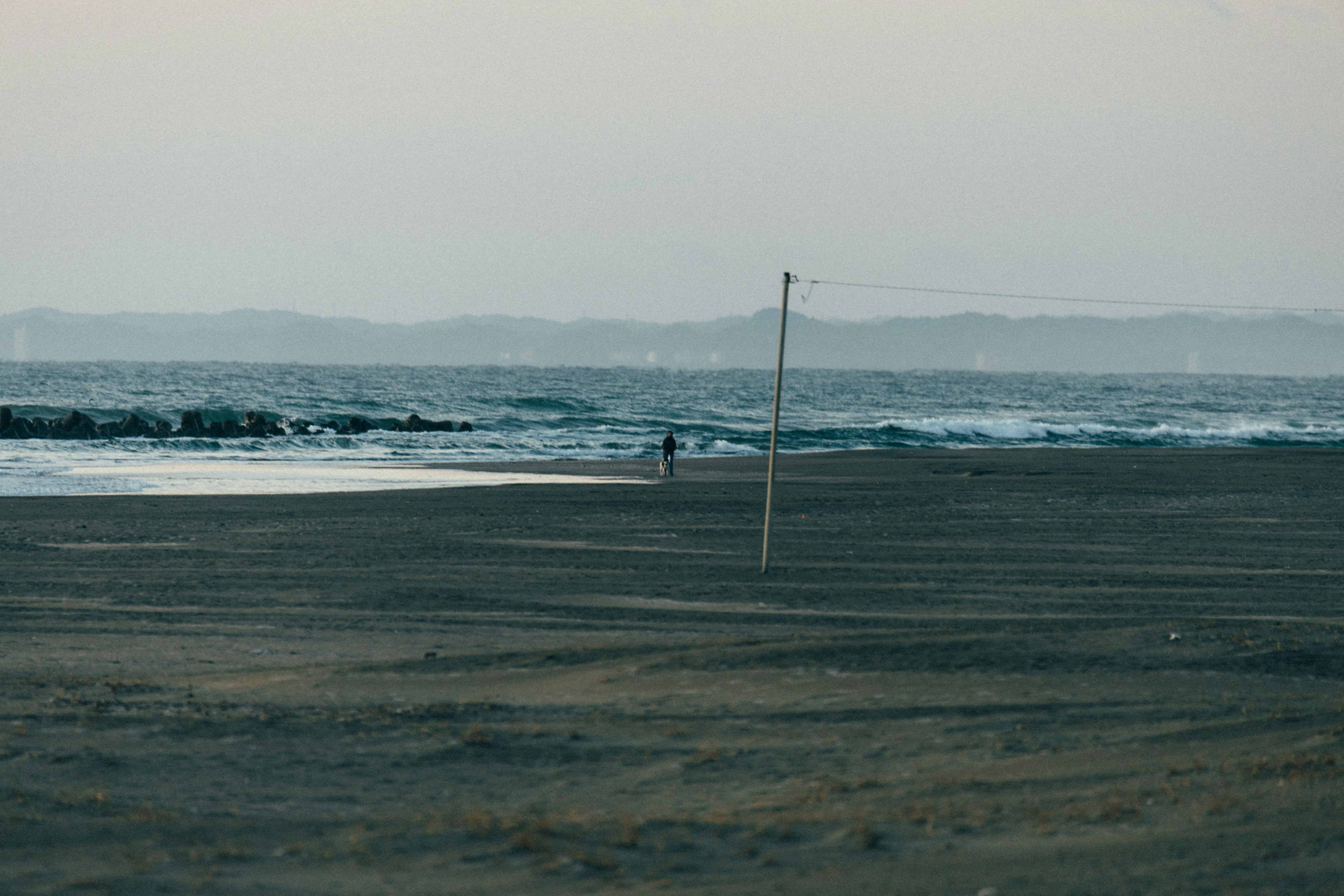 A person strolls on a sandy beach at dusk.