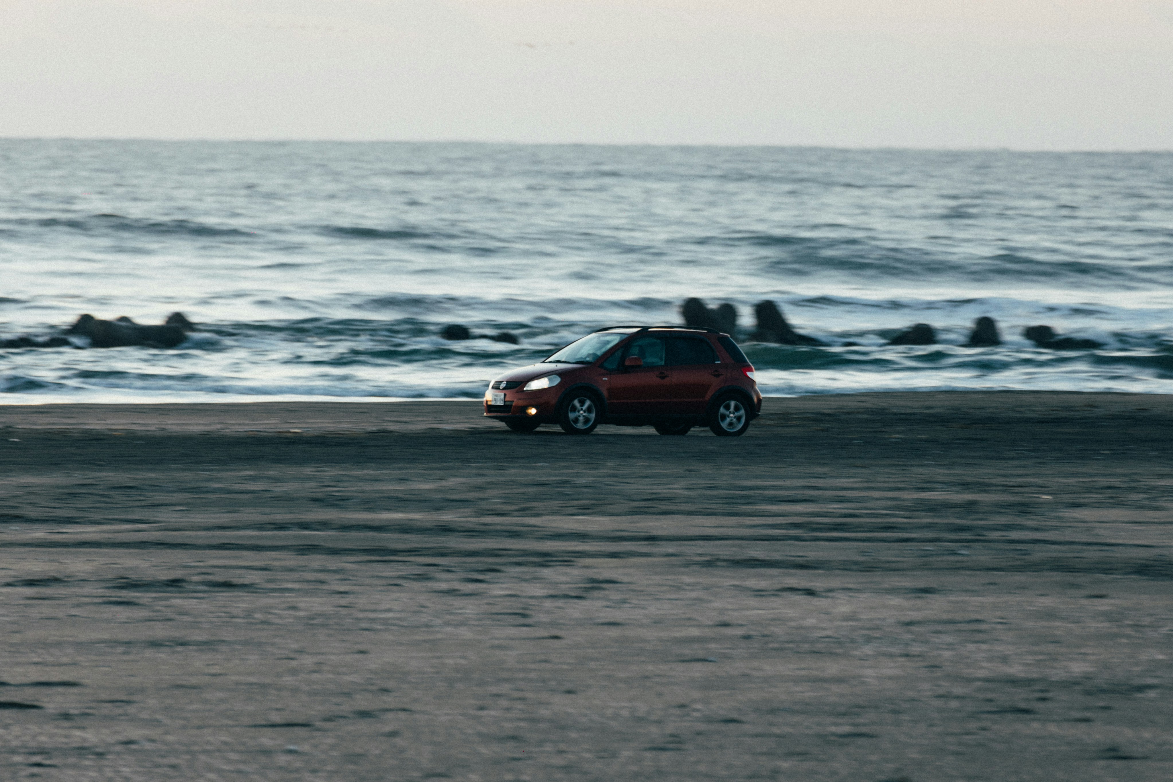 A red car drives on the beach.