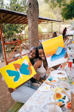 Two women smile while holding their paintings.
