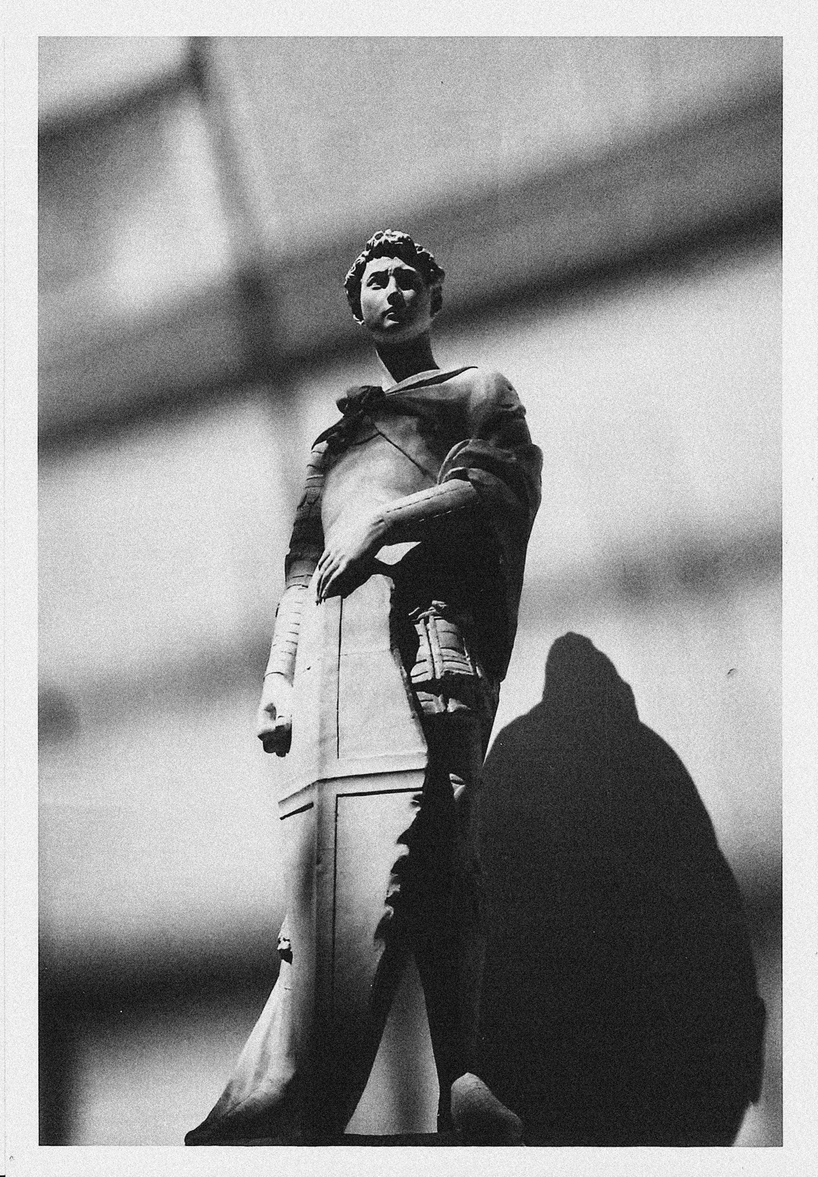 Uma estátua está de pé, lançando uma sombra longa e dramática.