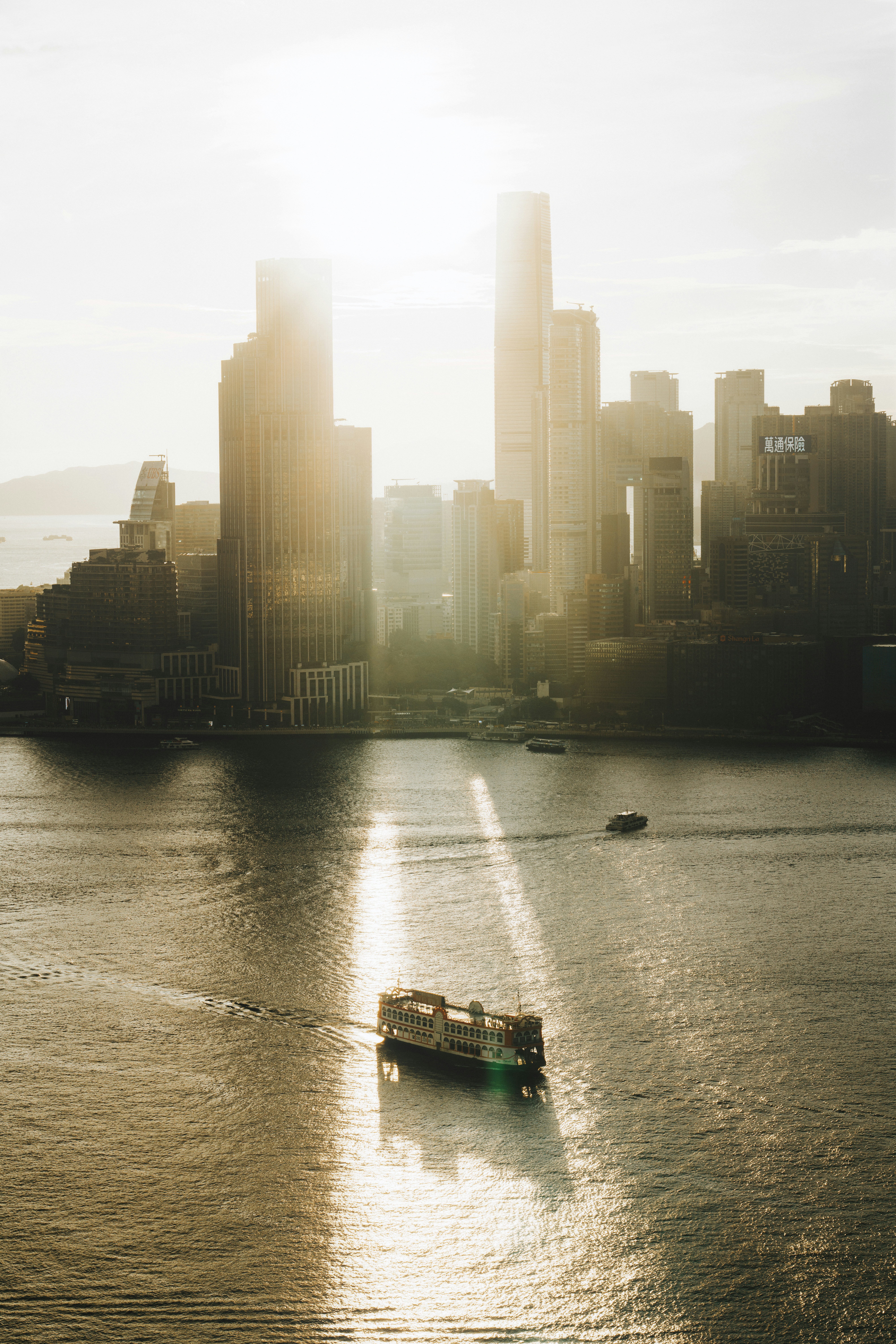A ferry travels on water in front of city buildings.