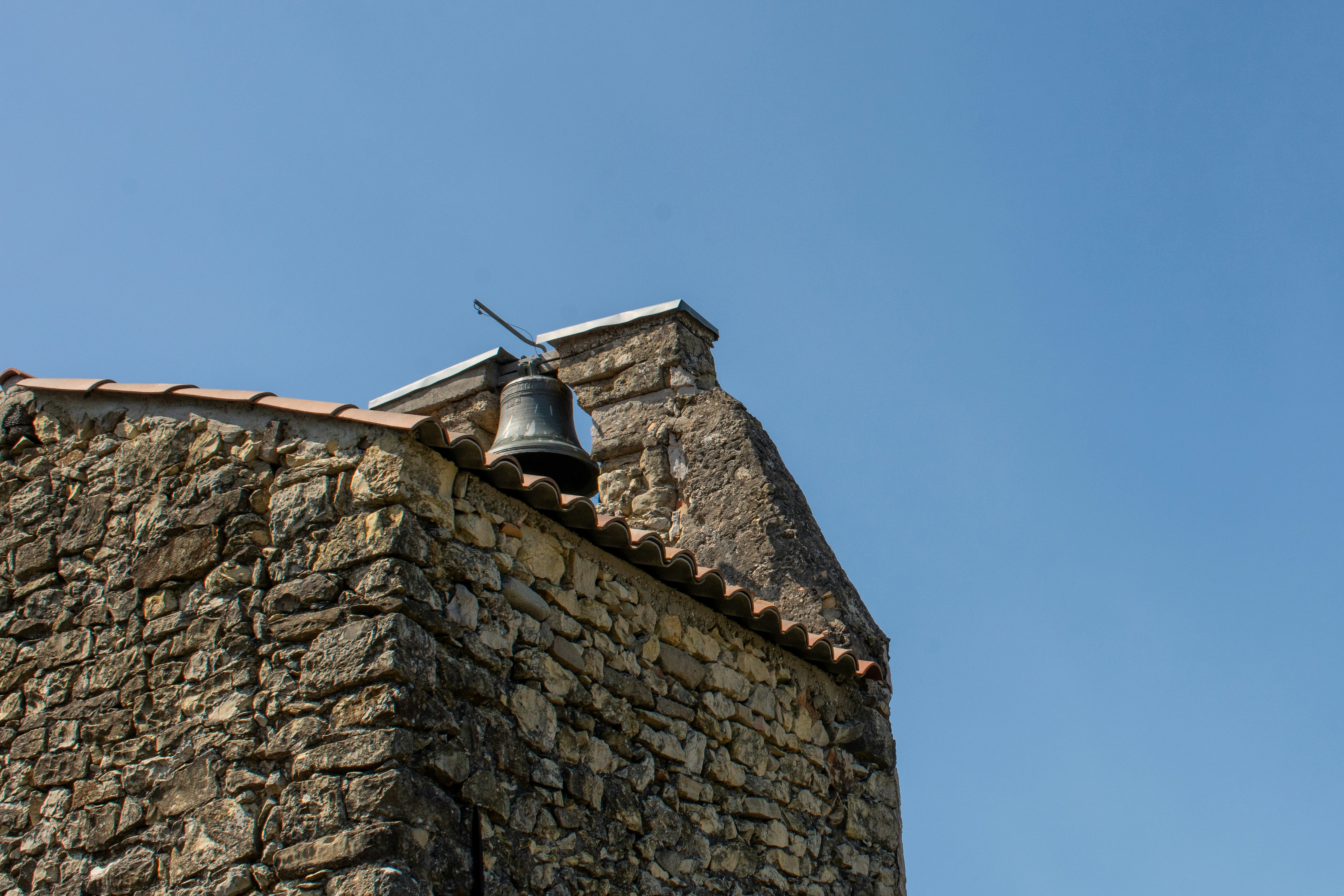A stone building bears a bell against blue sky.
