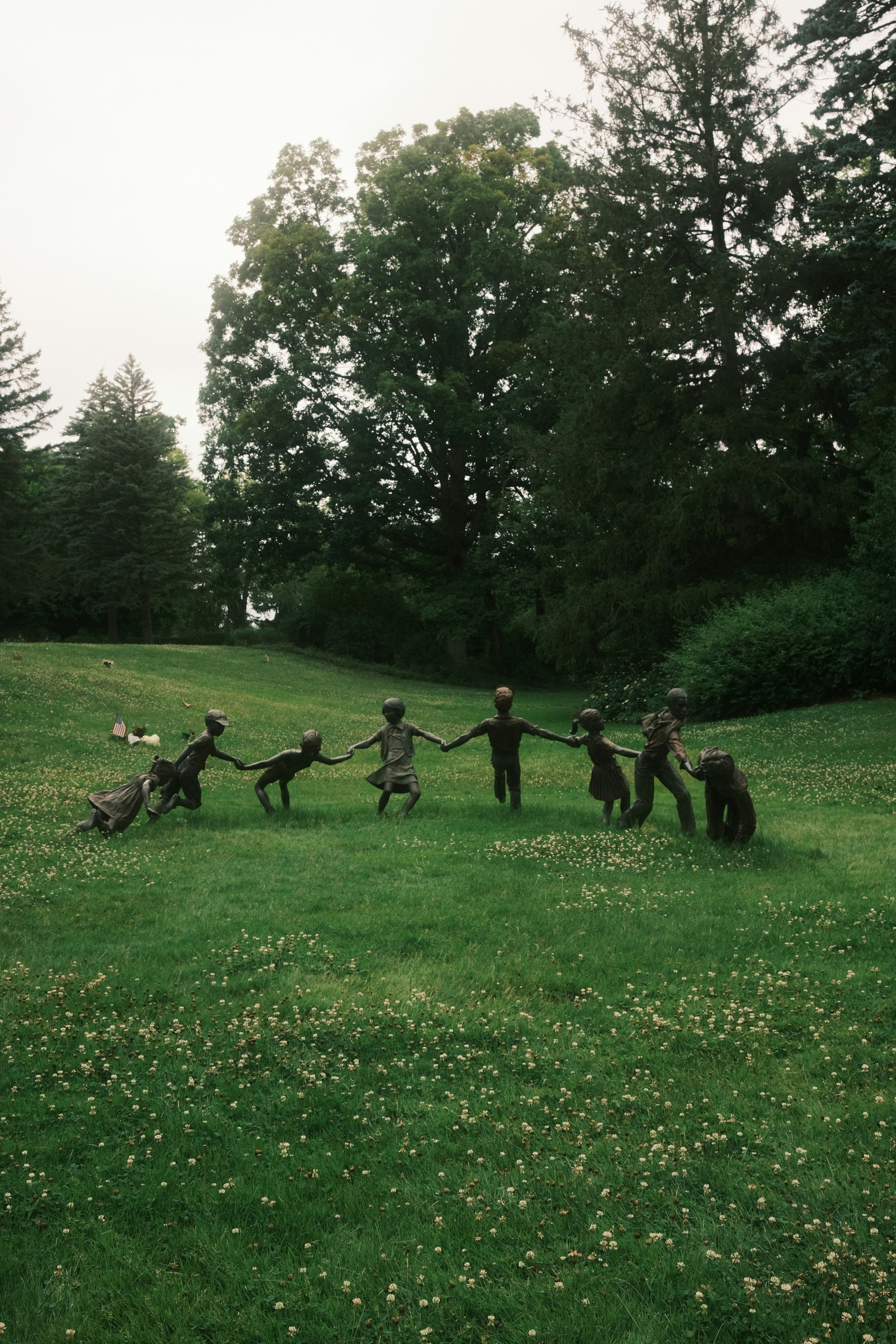Children sculptures hold hands on a grassy field.