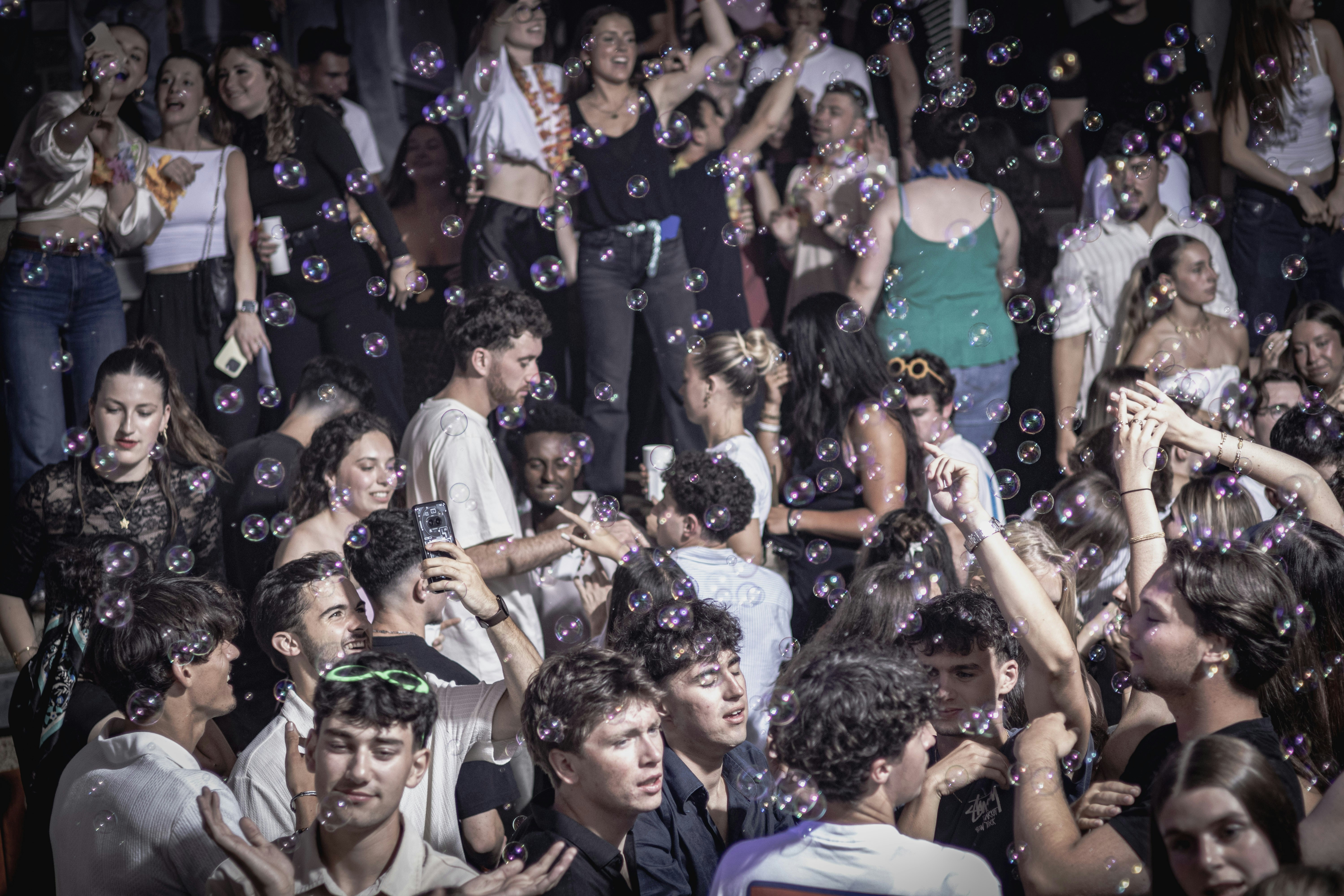 People are dancing in a crowded club with bubbles.