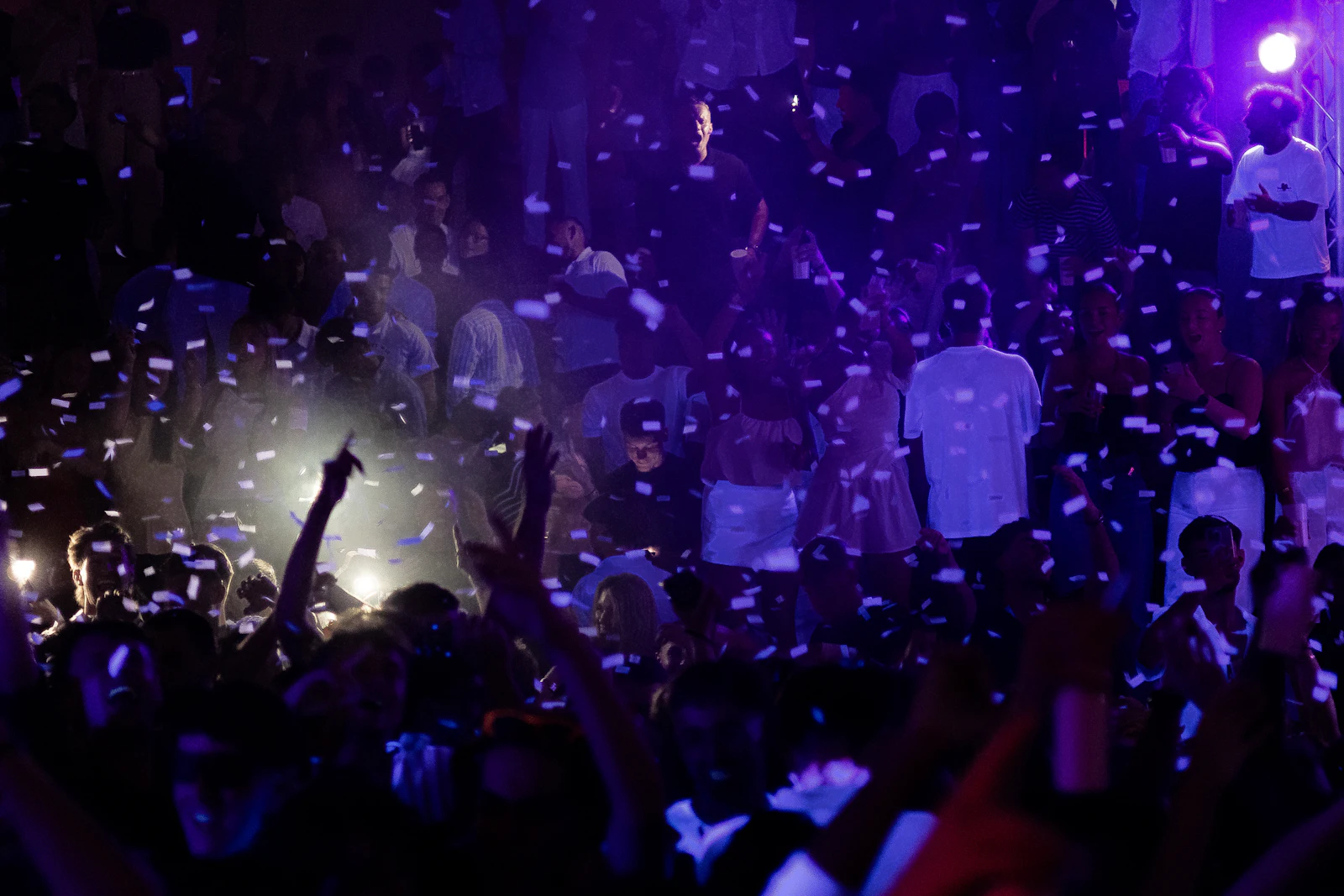 Crowd dancing under confetti and purple lights
