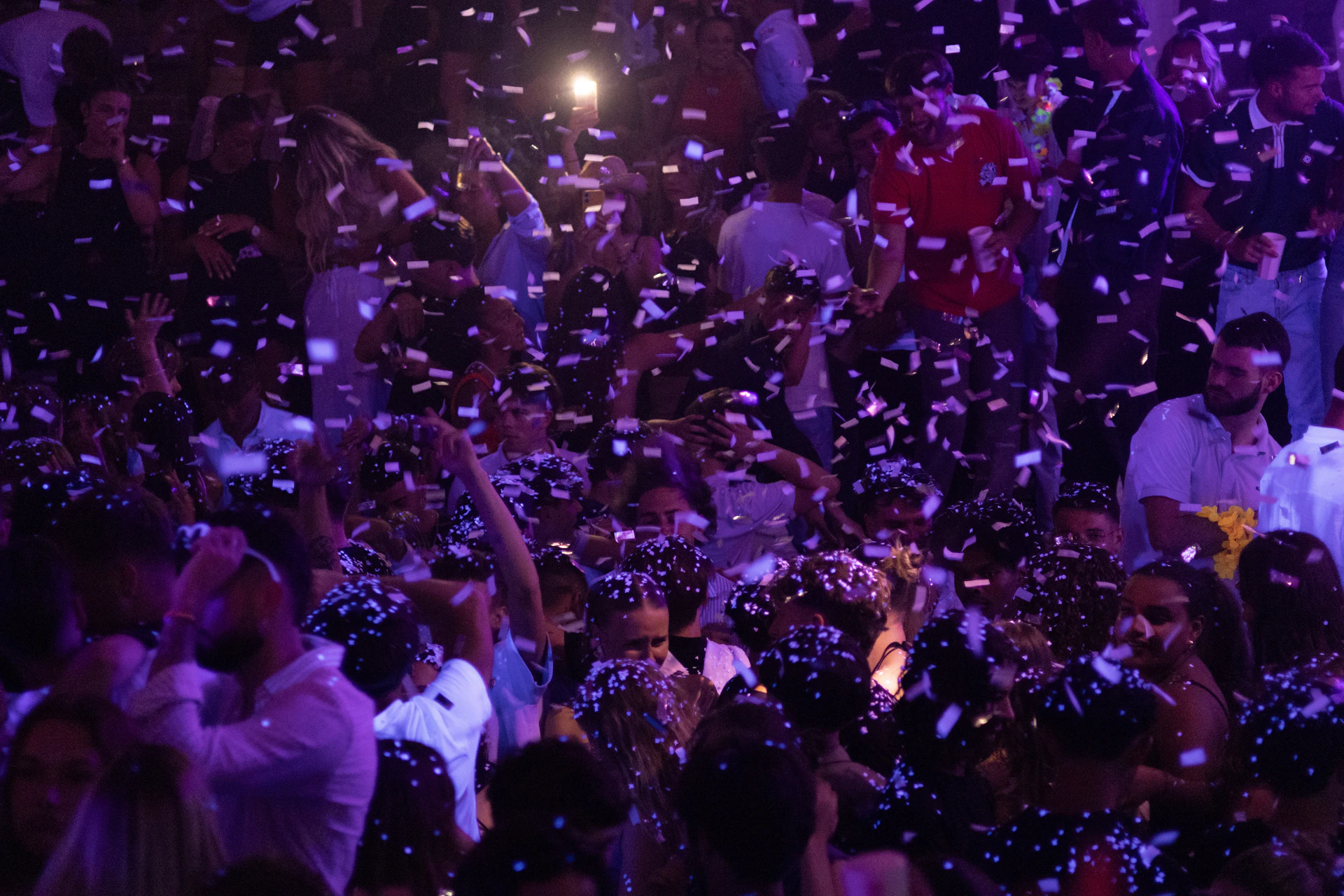 People dance amidst falling confetti at a club.