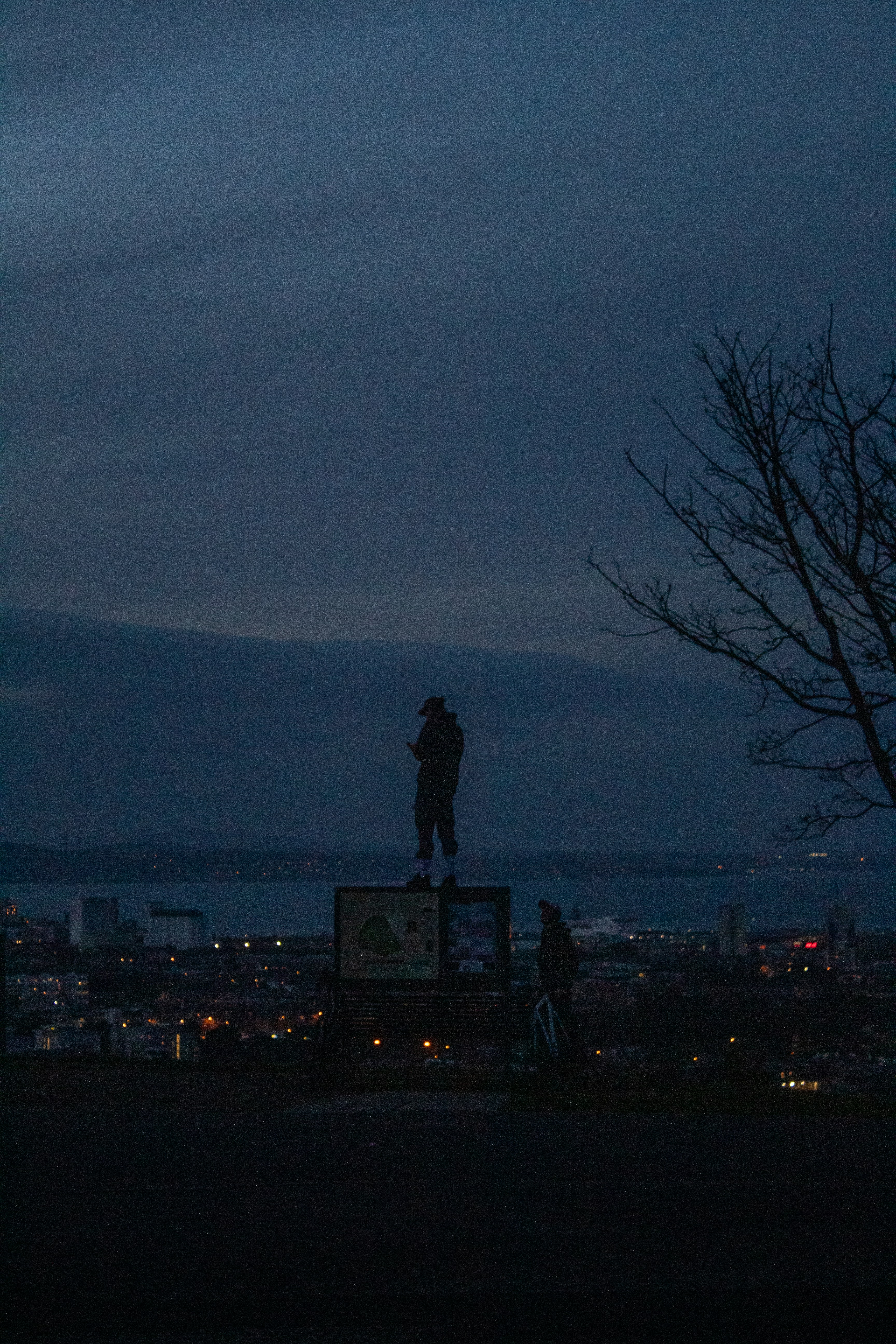Person stands atop a sign overlooking a city at dusk. photo – Free ...