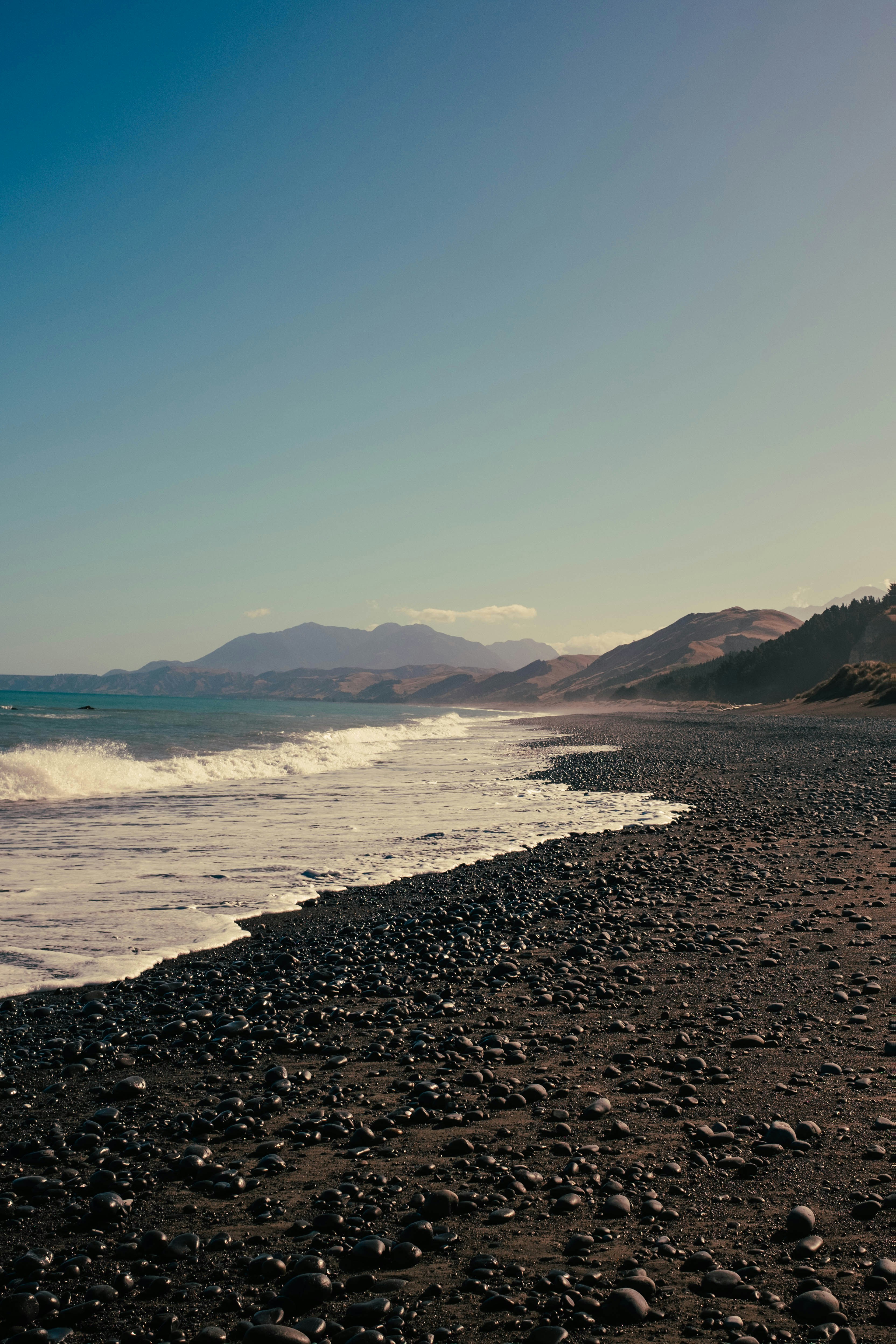 Waves crash on a black pebble beach.