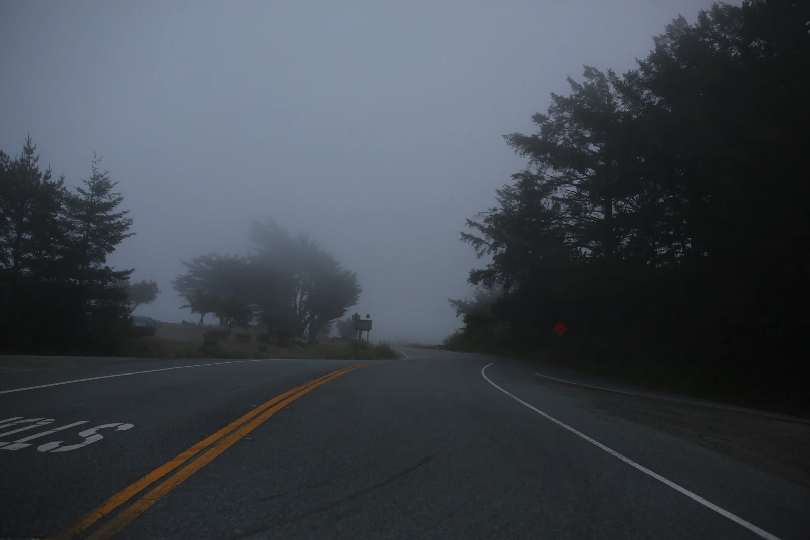A road curving into dense fog, the path ahead entirely obscured