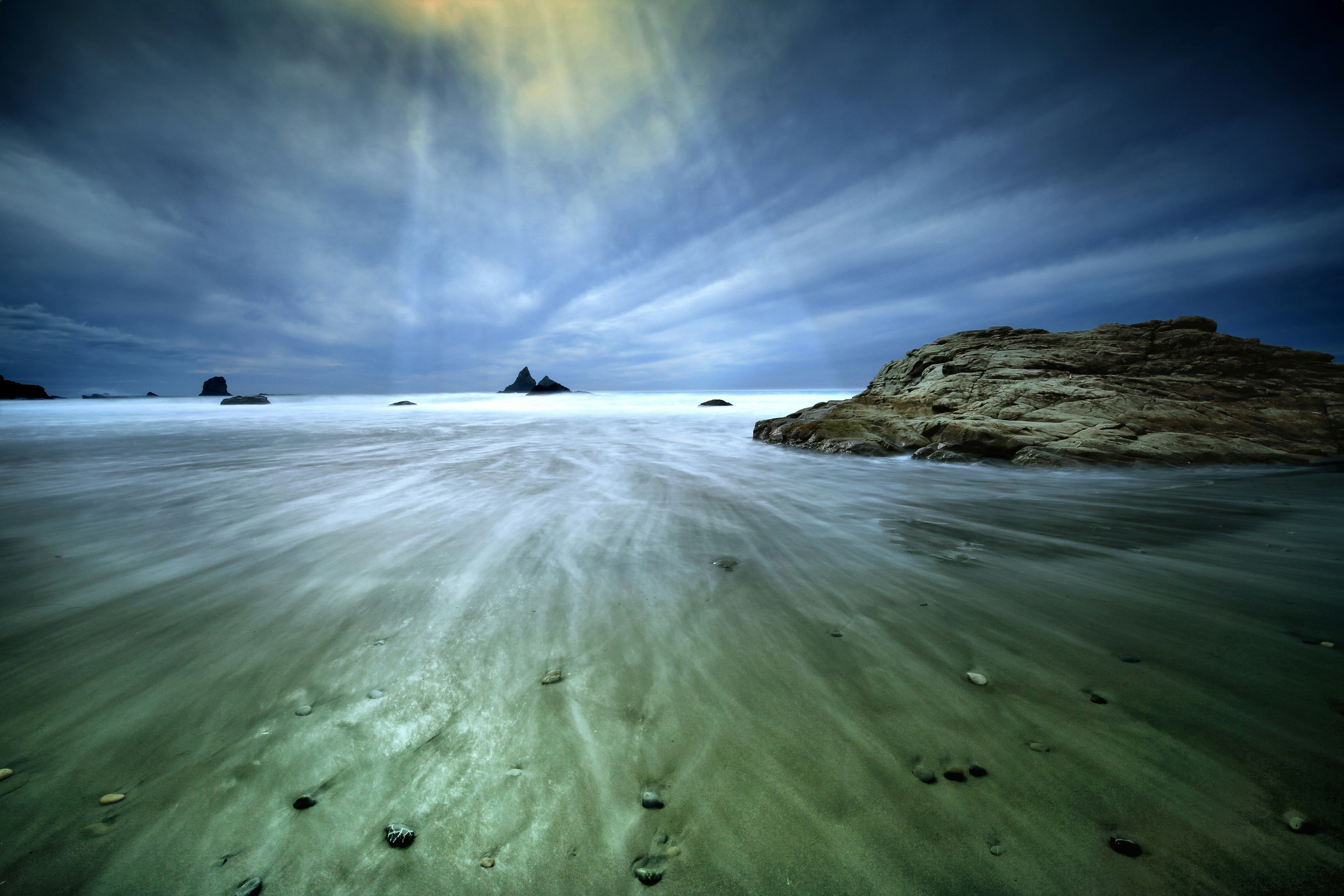 Waves wash over the beach under a moody sky.