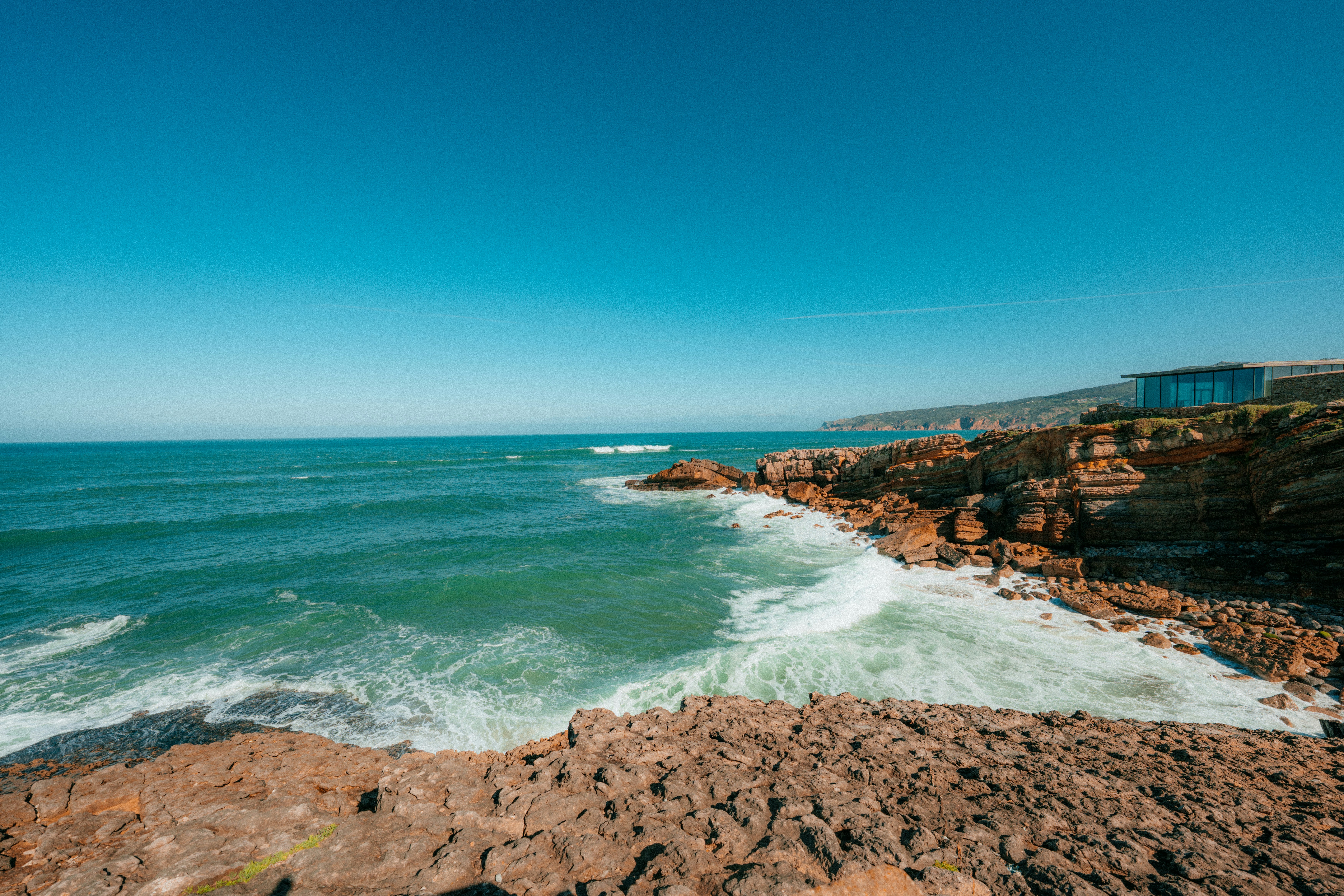 Rocky coastline with ocean waves under blue sky.