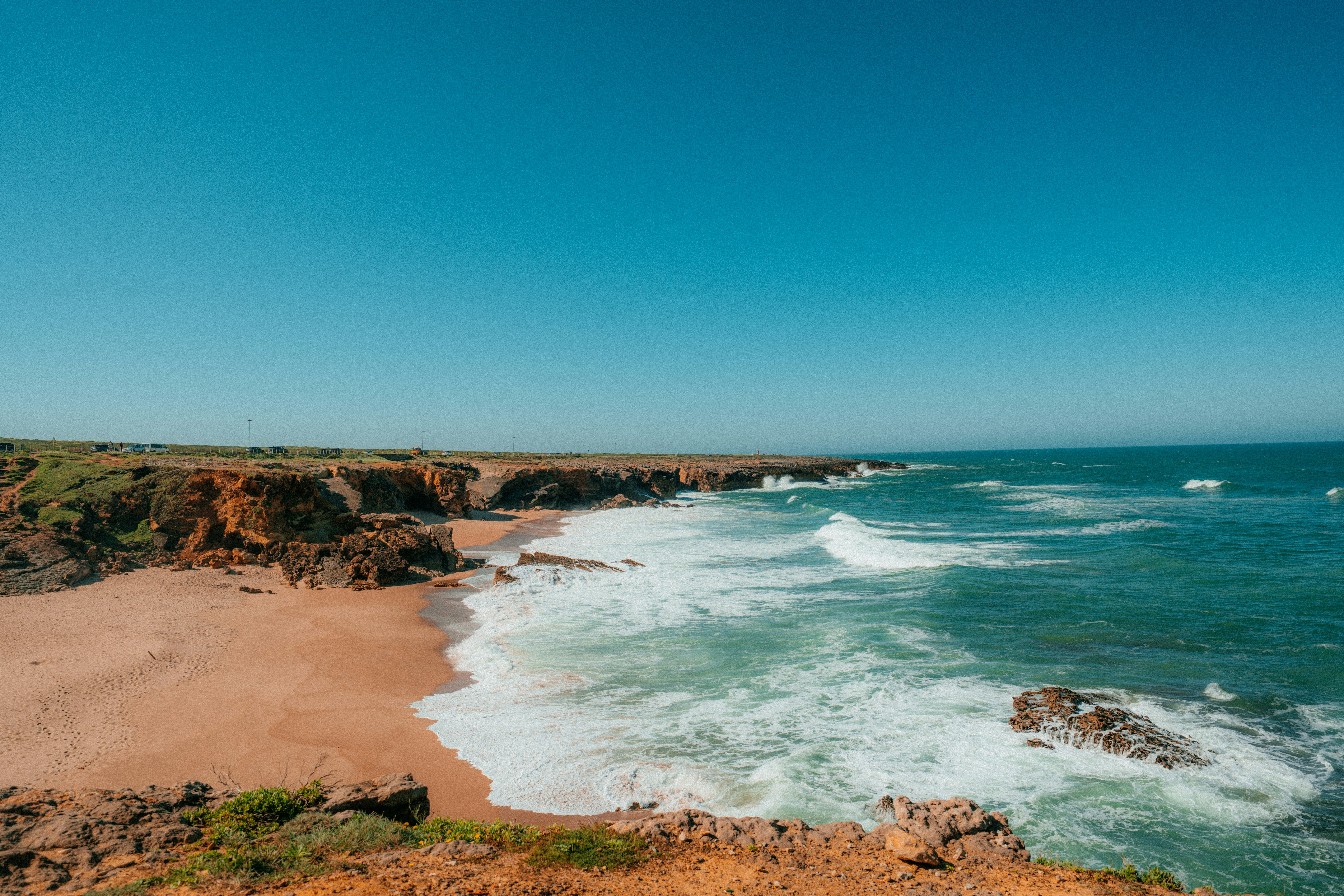Waves crash onto a rocky coastline under a blue sky.