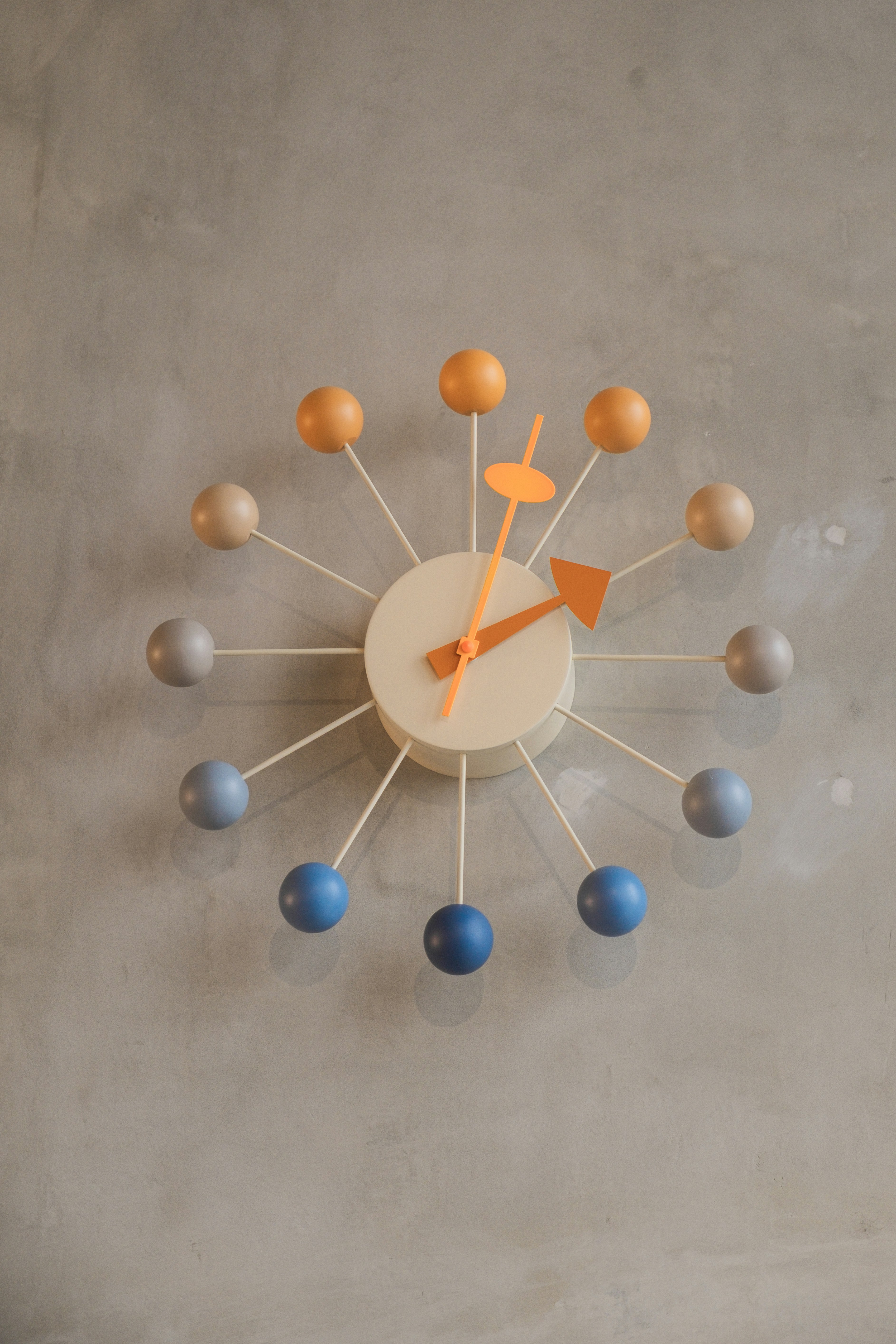 A colorful clock is hanging on a grey wall.