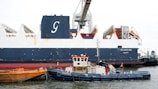 A tugboat works near a large cargo ship.