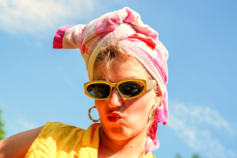 Woman poses with sunglasses and a head wrap.