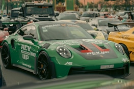 A green porsche is parked among other cars.