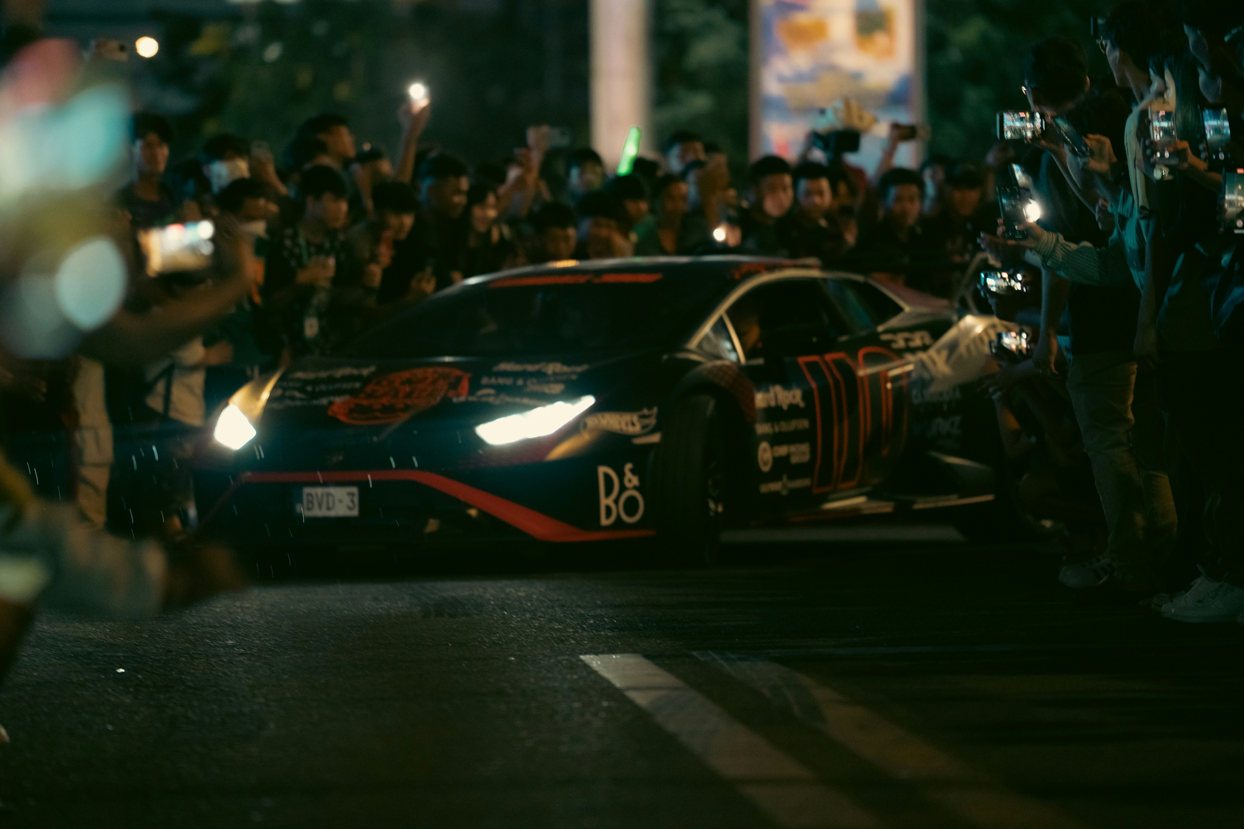 A race car drives through a crowded street at night.