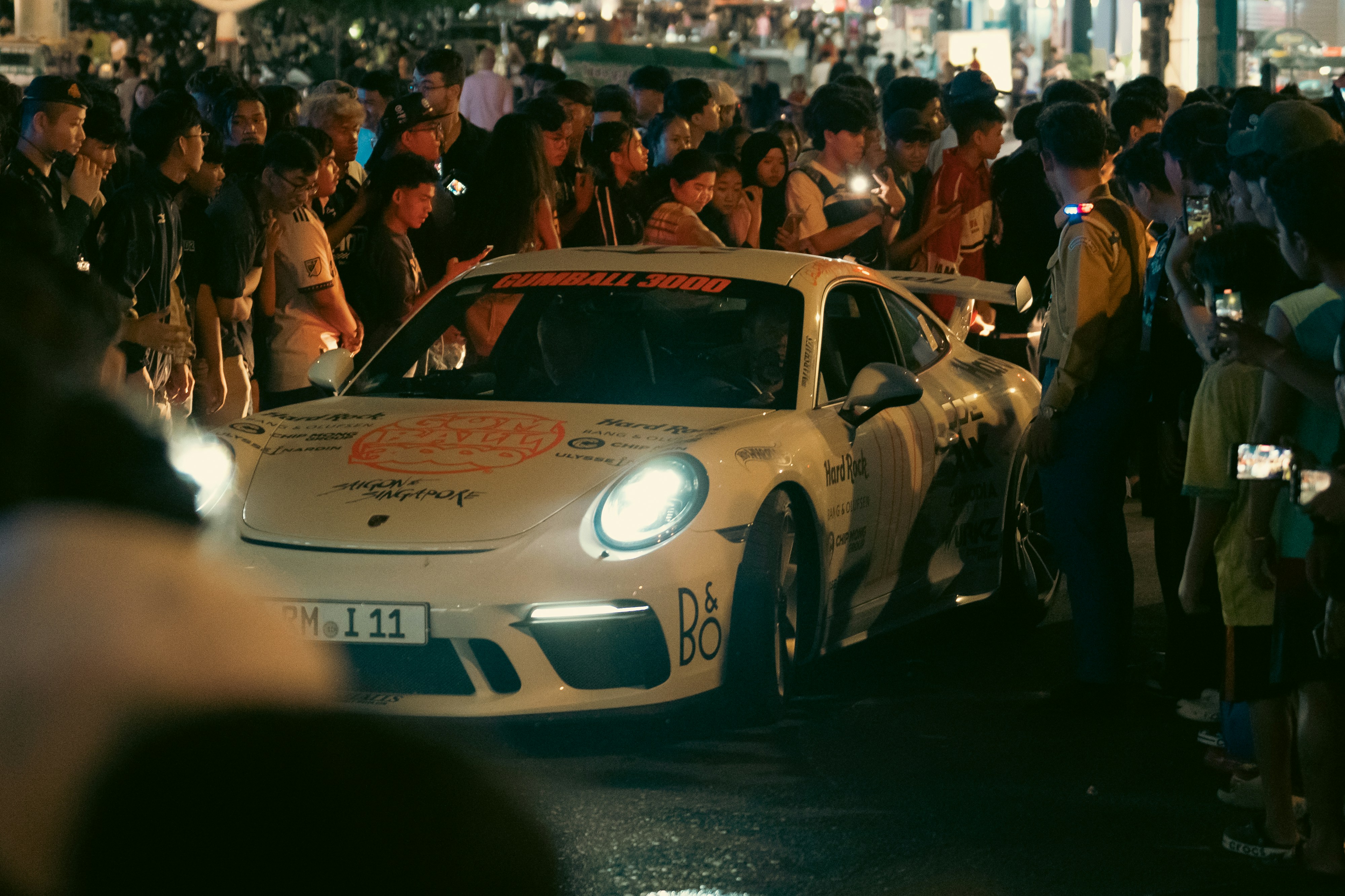 A crowd gathers around a white sports car.