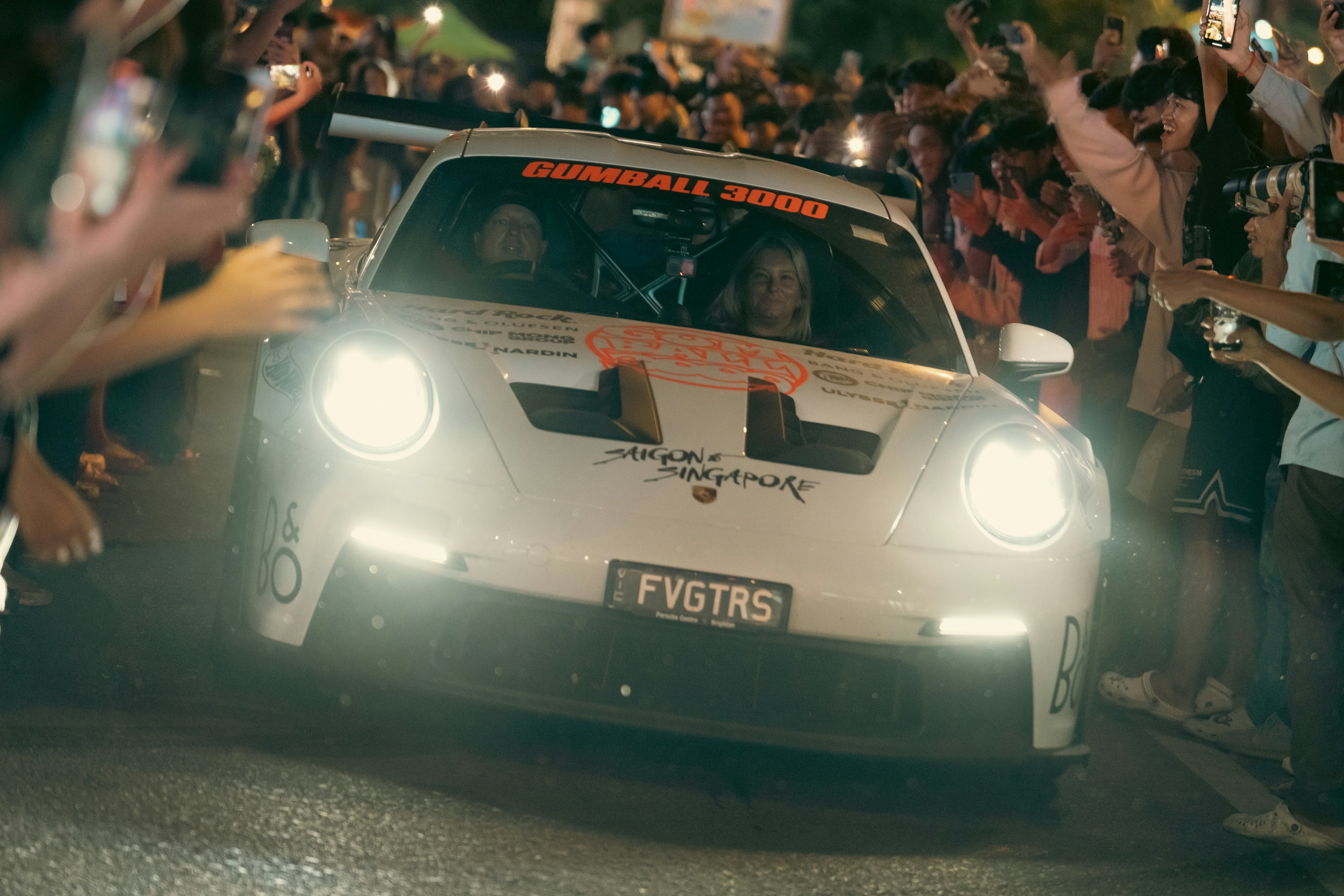 A white sports car drives through a crowd.