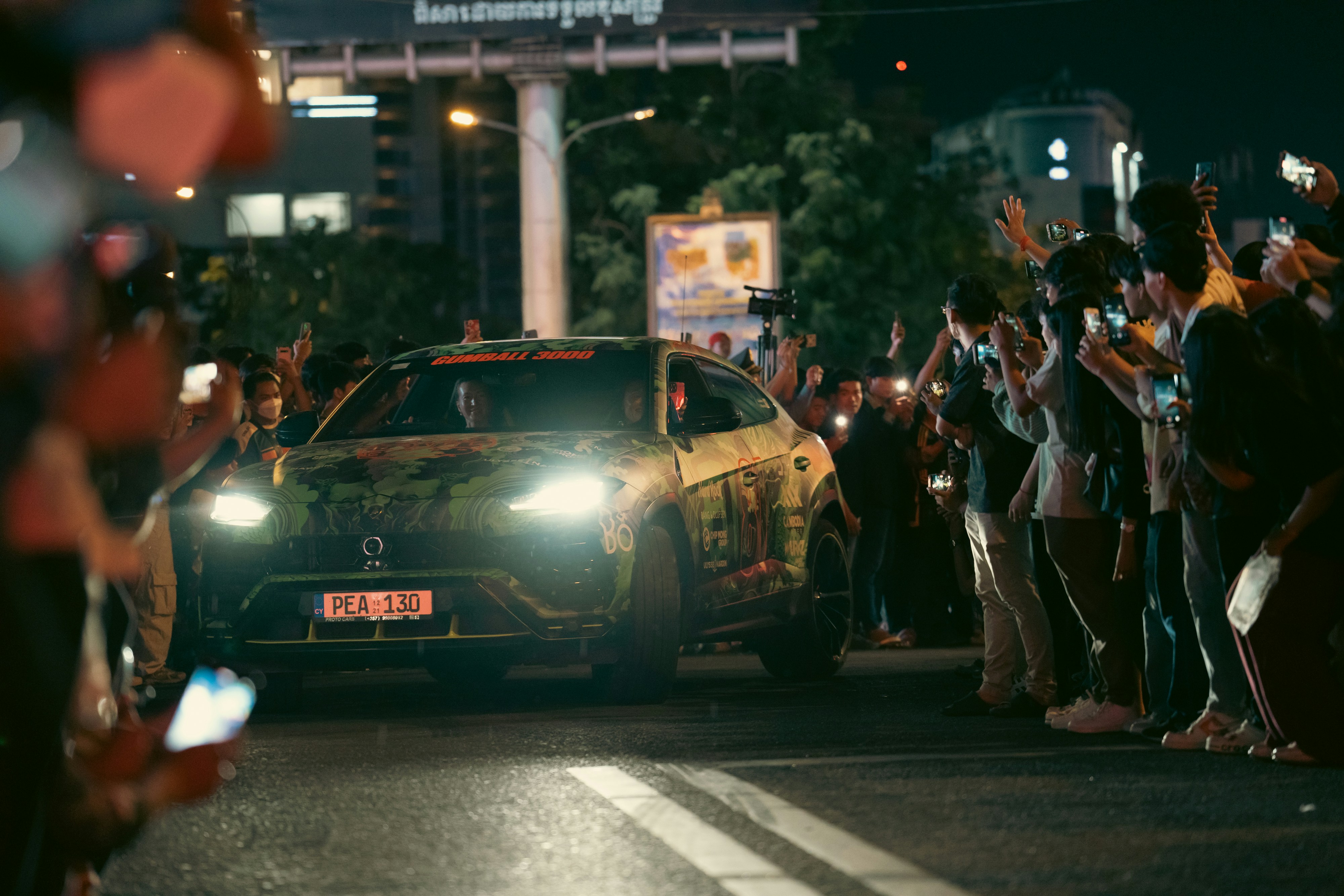 A crowd cheers on a car at night.