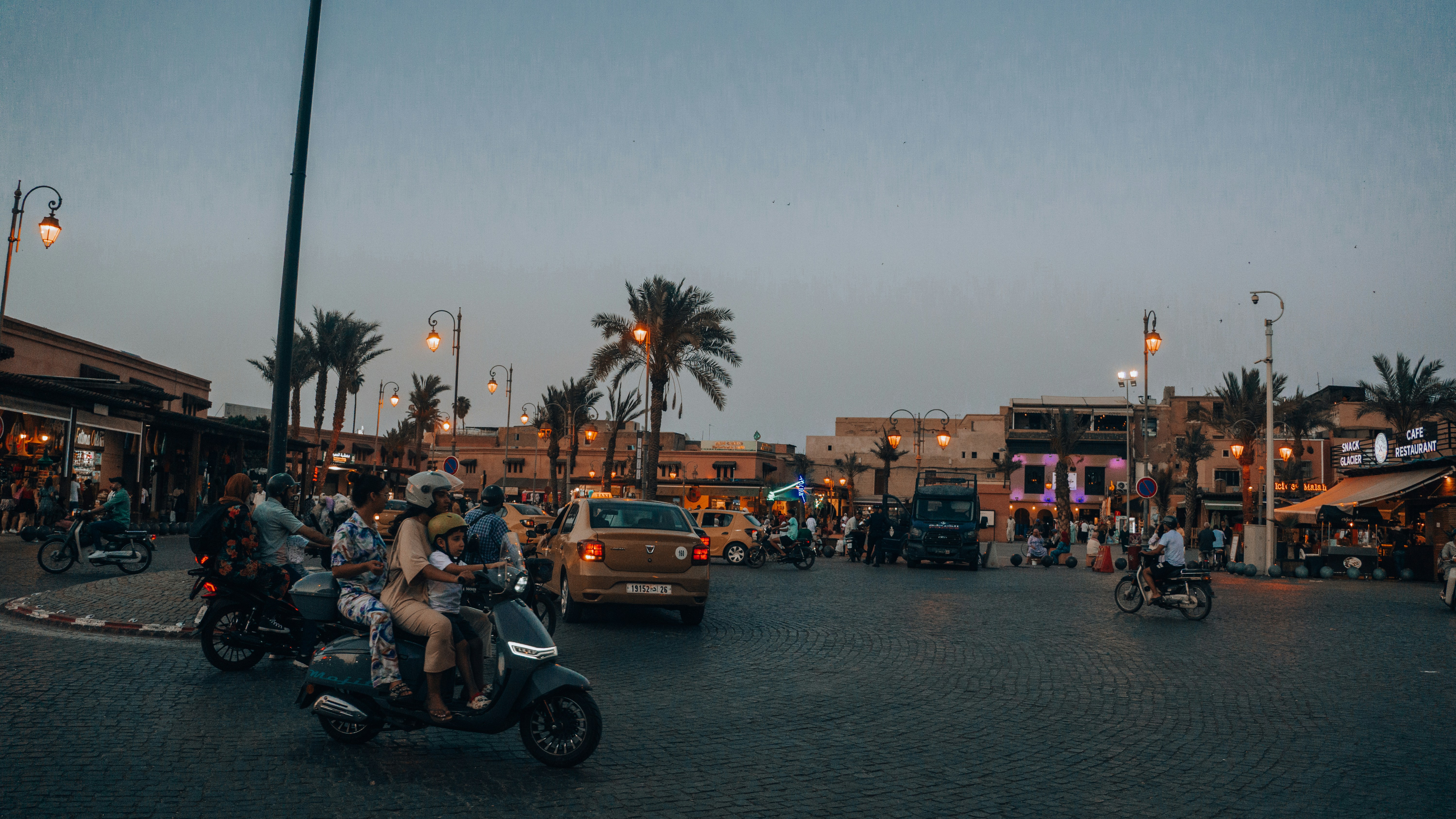 Busy street with scooters and buildings at dusk.