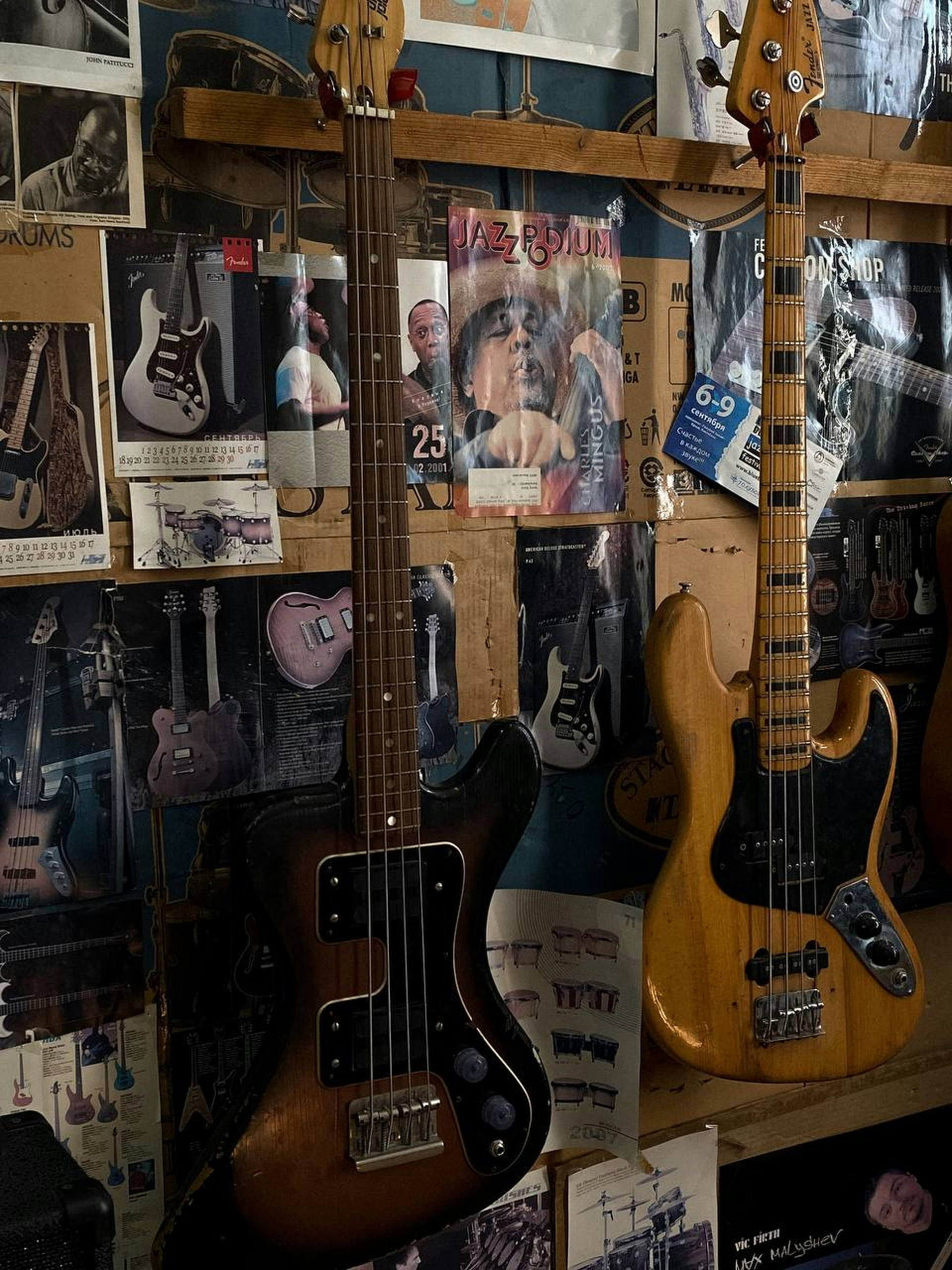 Two bass guitars stand in front of a wall.