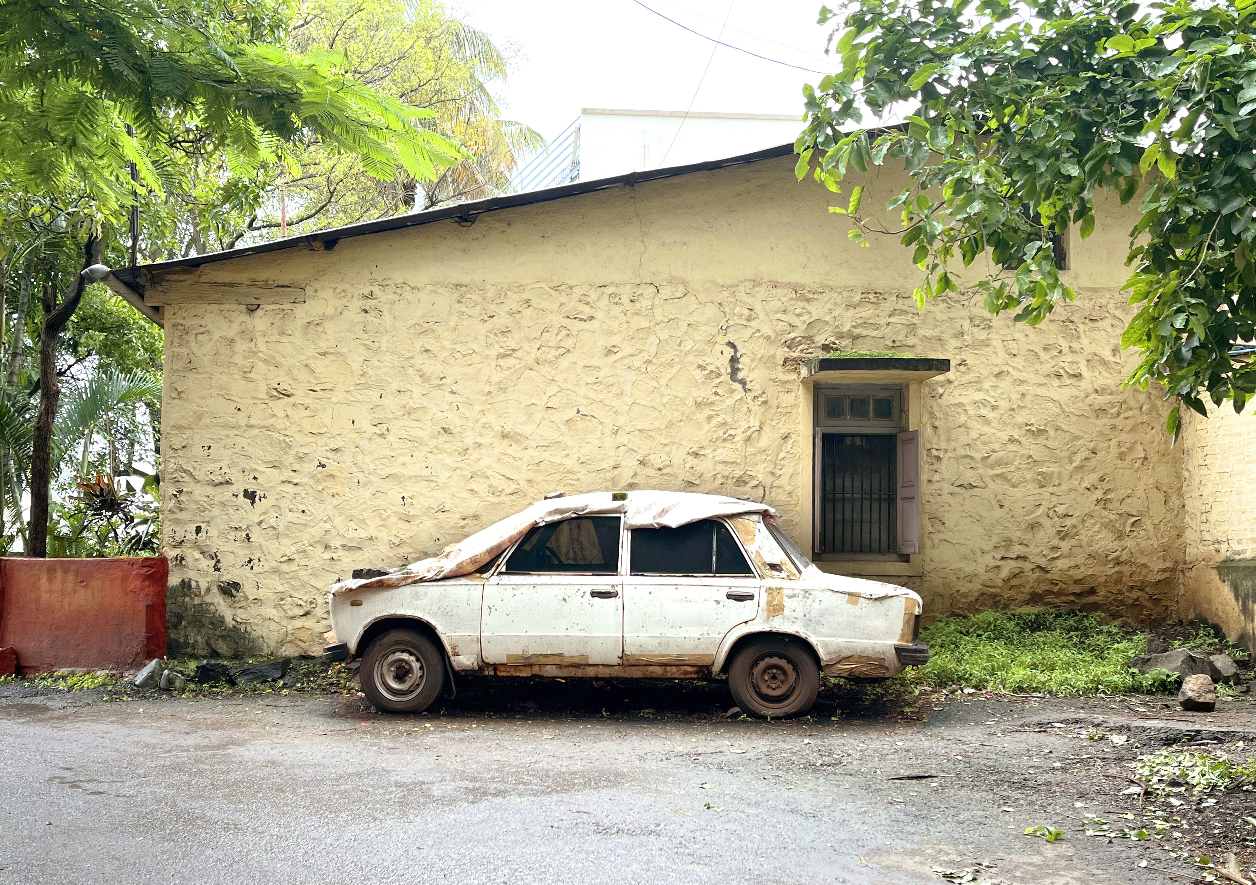 Old, beat-up car sits next to a building.