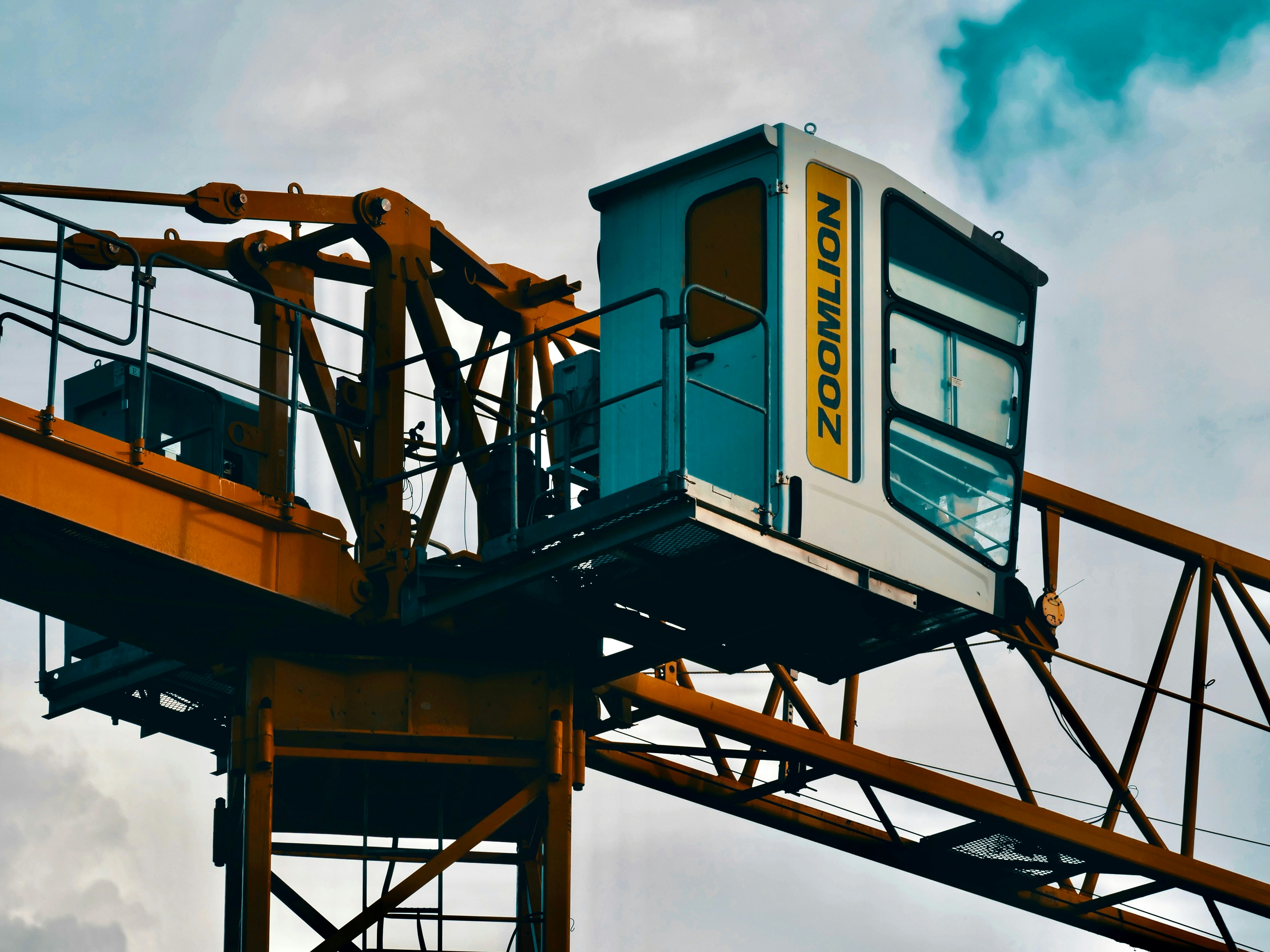 A construction crane's cab against a cloudy sky.