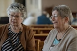 Two elderly women converse indoors, possibly at church.