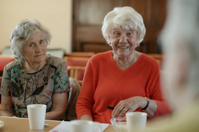 Two elderly women sit at a table, smiling