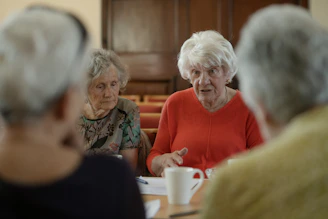Elderly women sit around a table, talking.