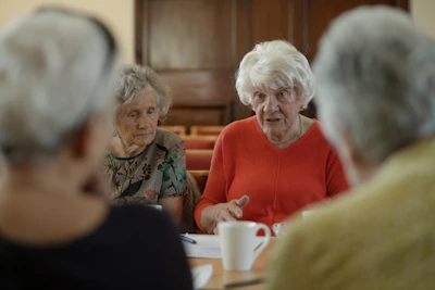 Elderly women sit around a table, talking.